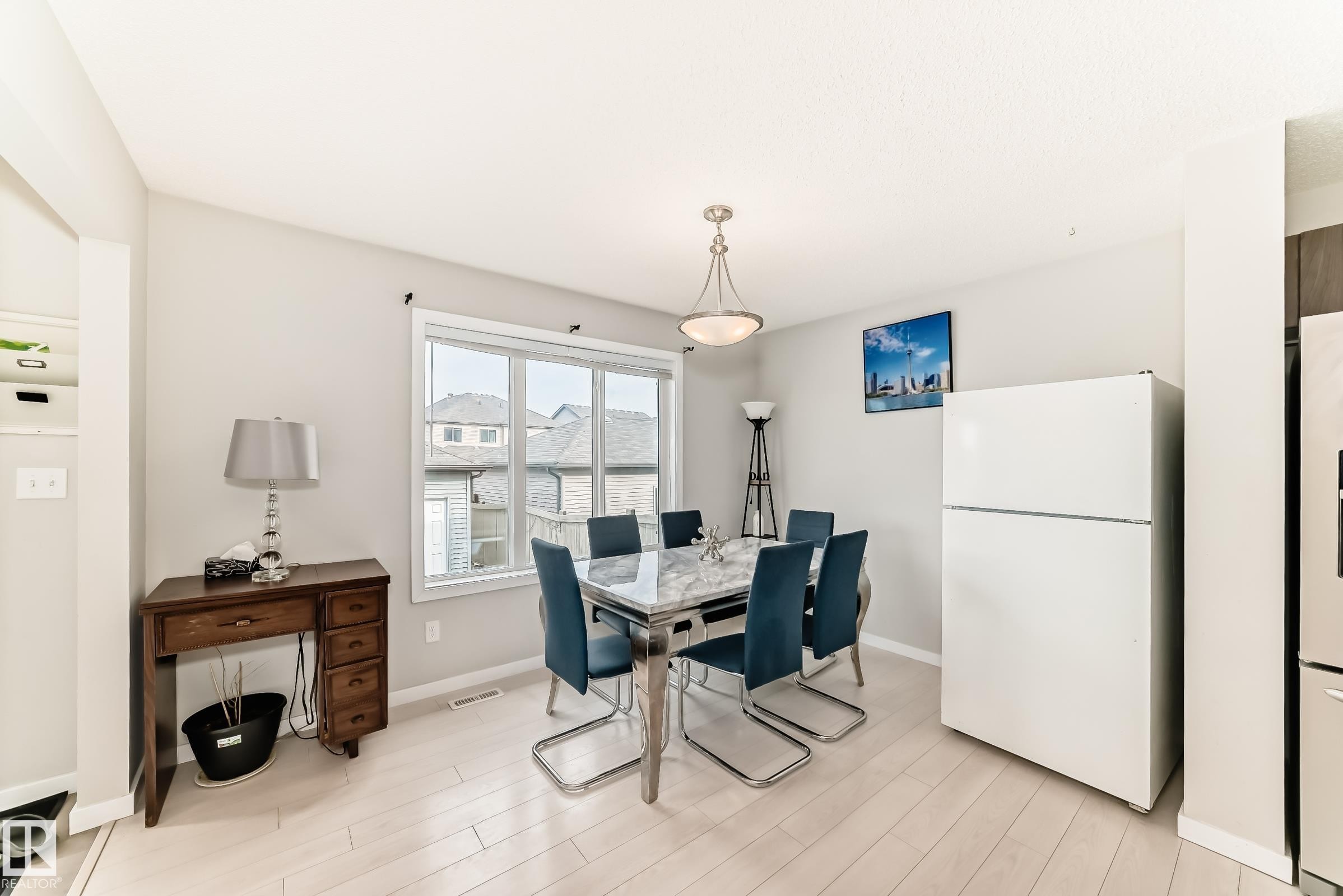 Bright dining area featuring wood-finish flooring, a contemporary ceiling light fixture, a large window with white trim, and light-toned wall paint - 328 Watt Boulevard, Edmonton, AB - Indoor Photo Showing Dining Room