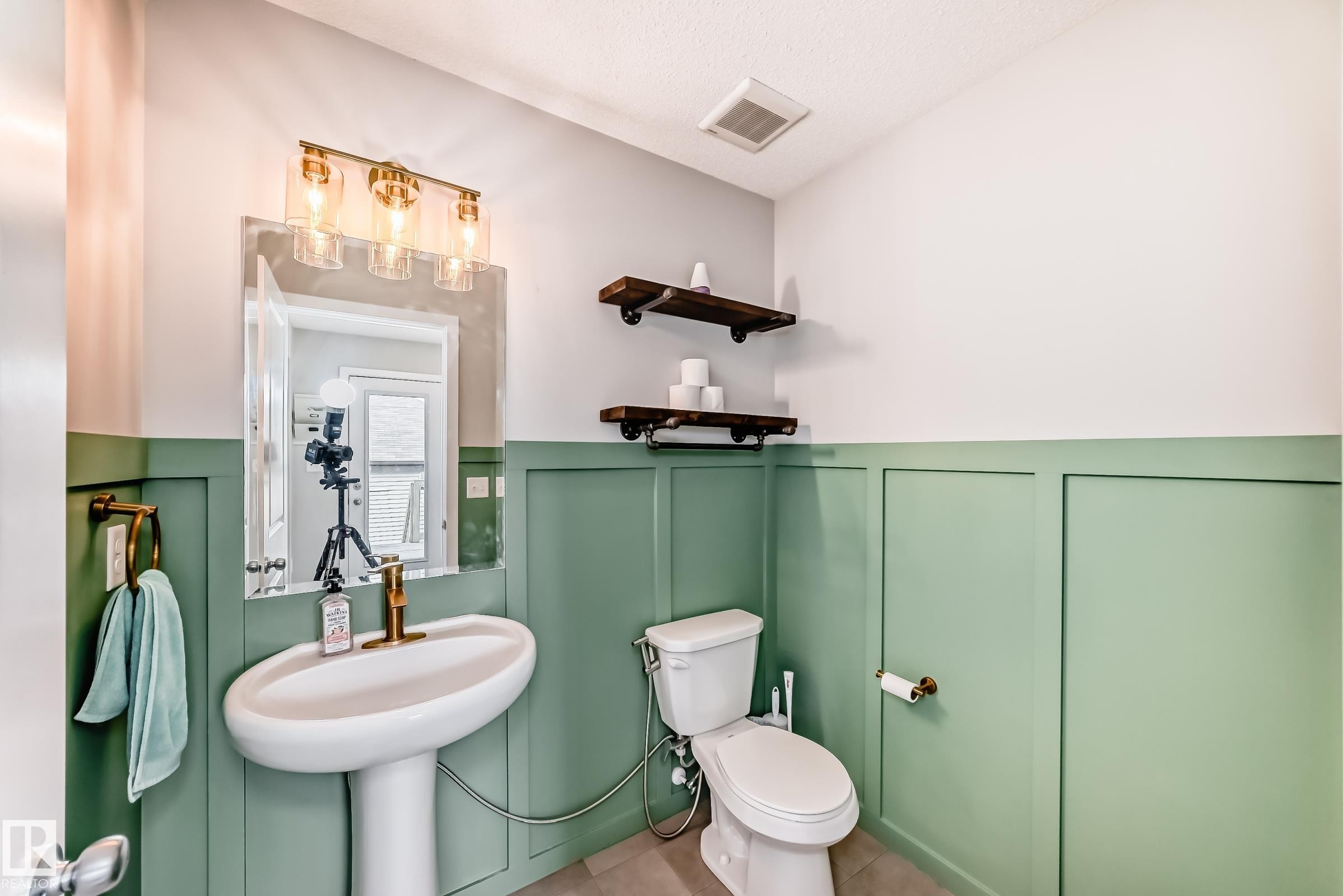 Powder room featuring green wainscoting, a pedestal sink with a brass-finish faucet, and a wall-mounted mirror with a 3-light vanity fixture - 328 Watt Boulevard, Edmonton, AB - Indoor Photo Showing Bathroom