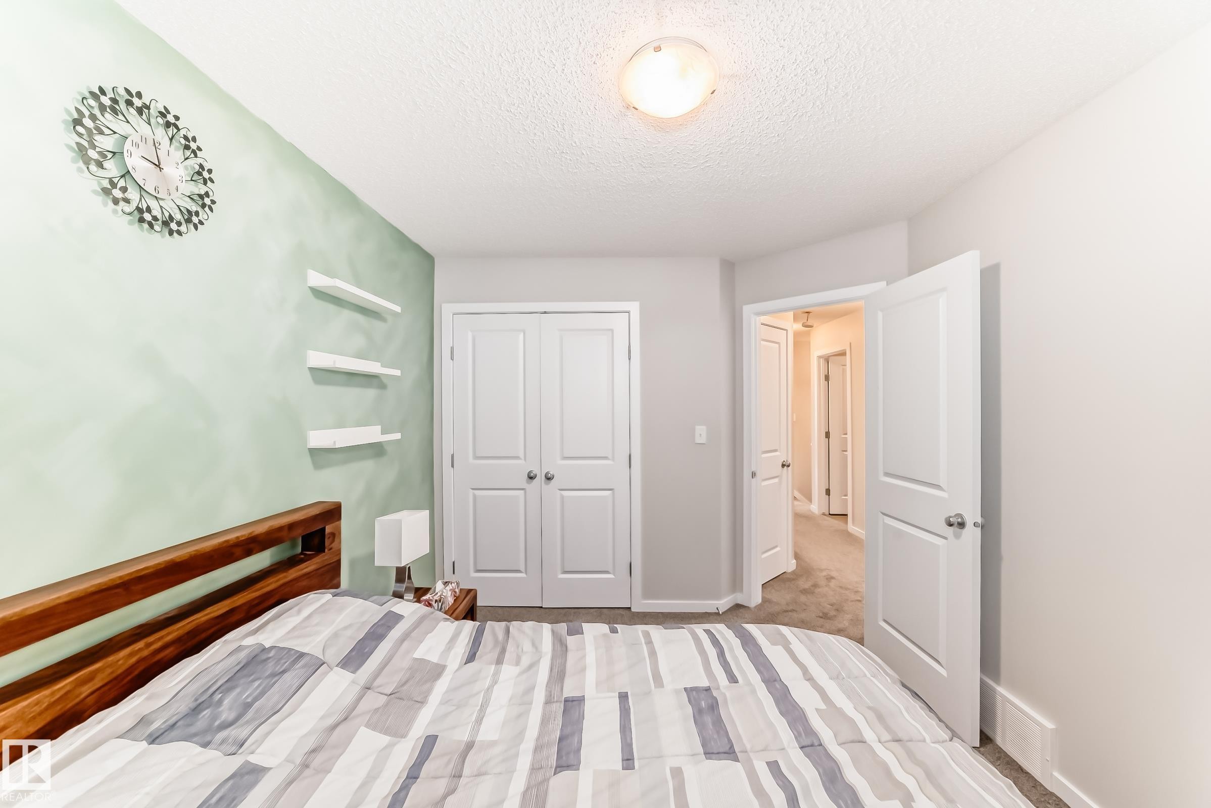 Carpeted room featuring a light green accent wall with three built-in floating shelves, white trim, and a ceiling-mounted light fixture - 328 Watt Boulevard, Edmonton, AB - Indoor Photo Showing Bedroom