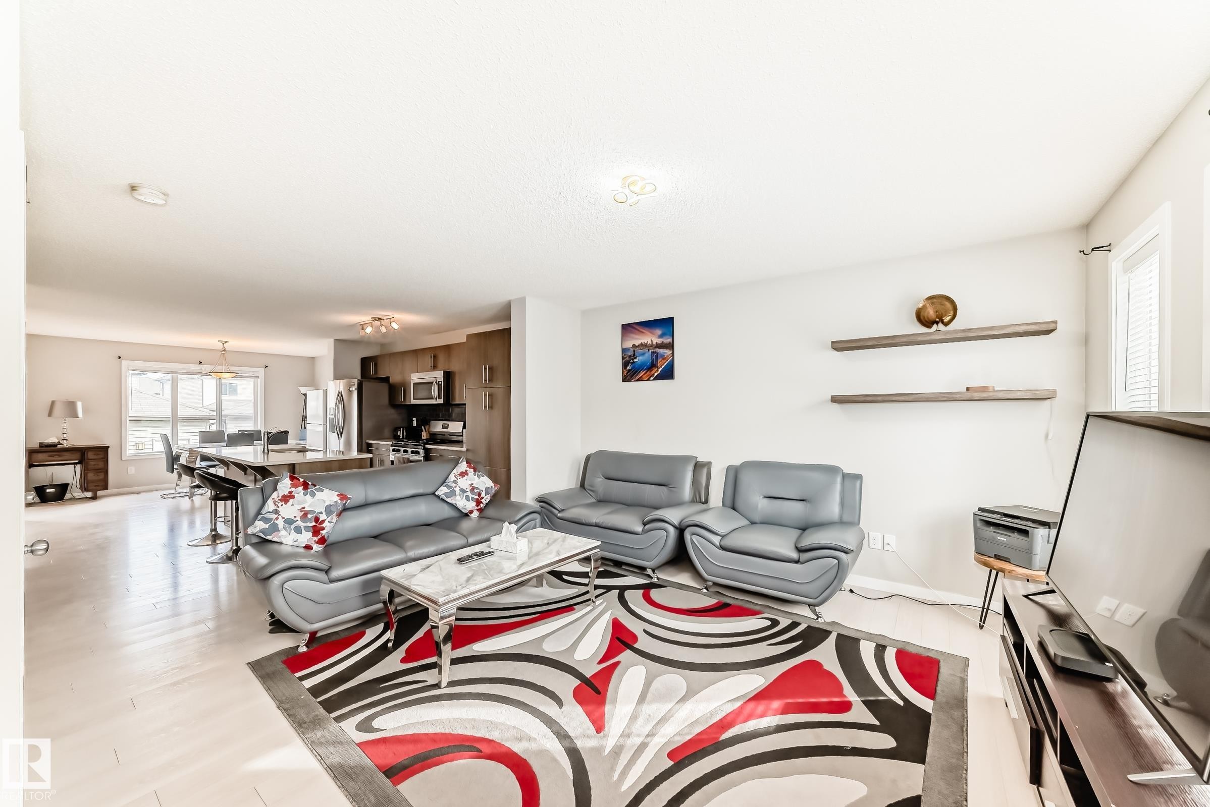 Open-concept living area featuring light wood-finish flooring, a kitchen with stainless steel appliances, and a breakfast bar with seating - 328 Watt Boulevard, Edmonton, AB - Indoor Photo Showing Living Room
