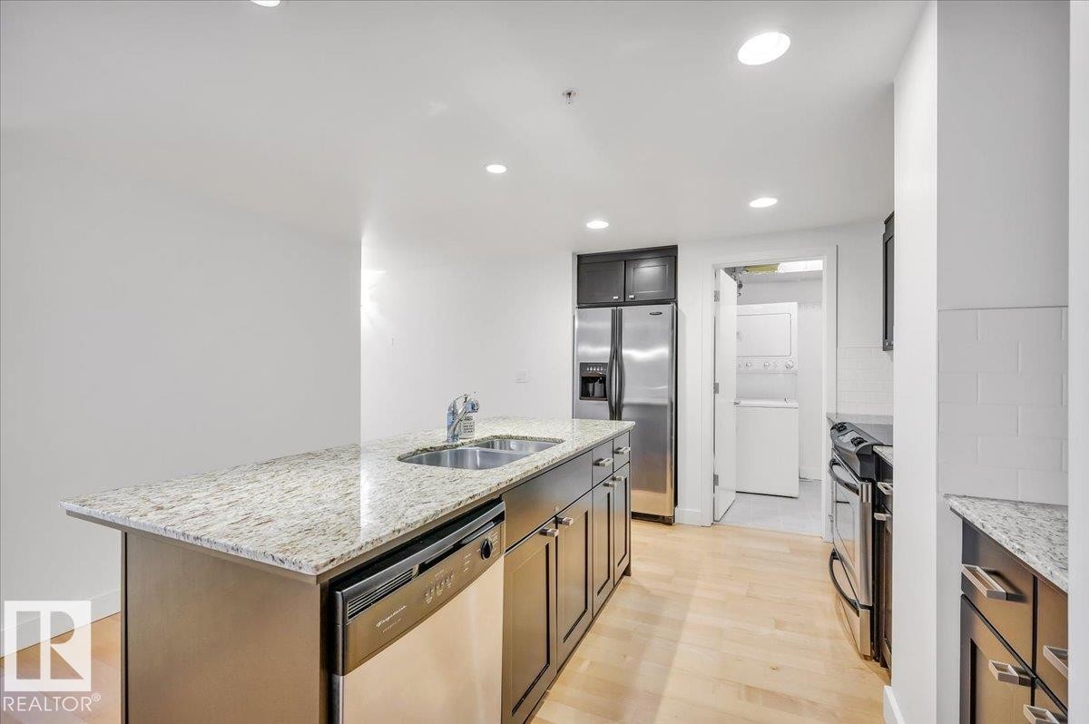 GRANITE COUNTERTOPS, LARGE ISLAND AND STAINLESS APPLIANCES IN THE SPACIOUS KITCHEN - 503 10028 119 Street, Edmonton, AB - Indoor Photo Showing Kitchen With Double Sink With Upgraded Kitchen