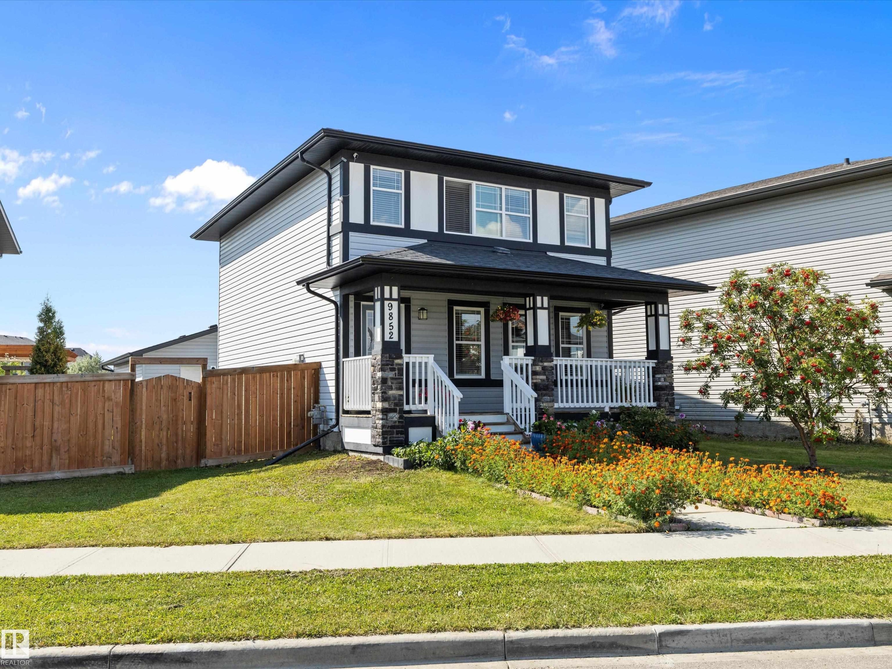 The property features a two-story exterior with light-colored siding and dark trim, a covered front porch with white railings, and stone accents on the porch pillars - 9852 217 Street, Edmonton, AB - Outdoor With Deck Patio Veranda