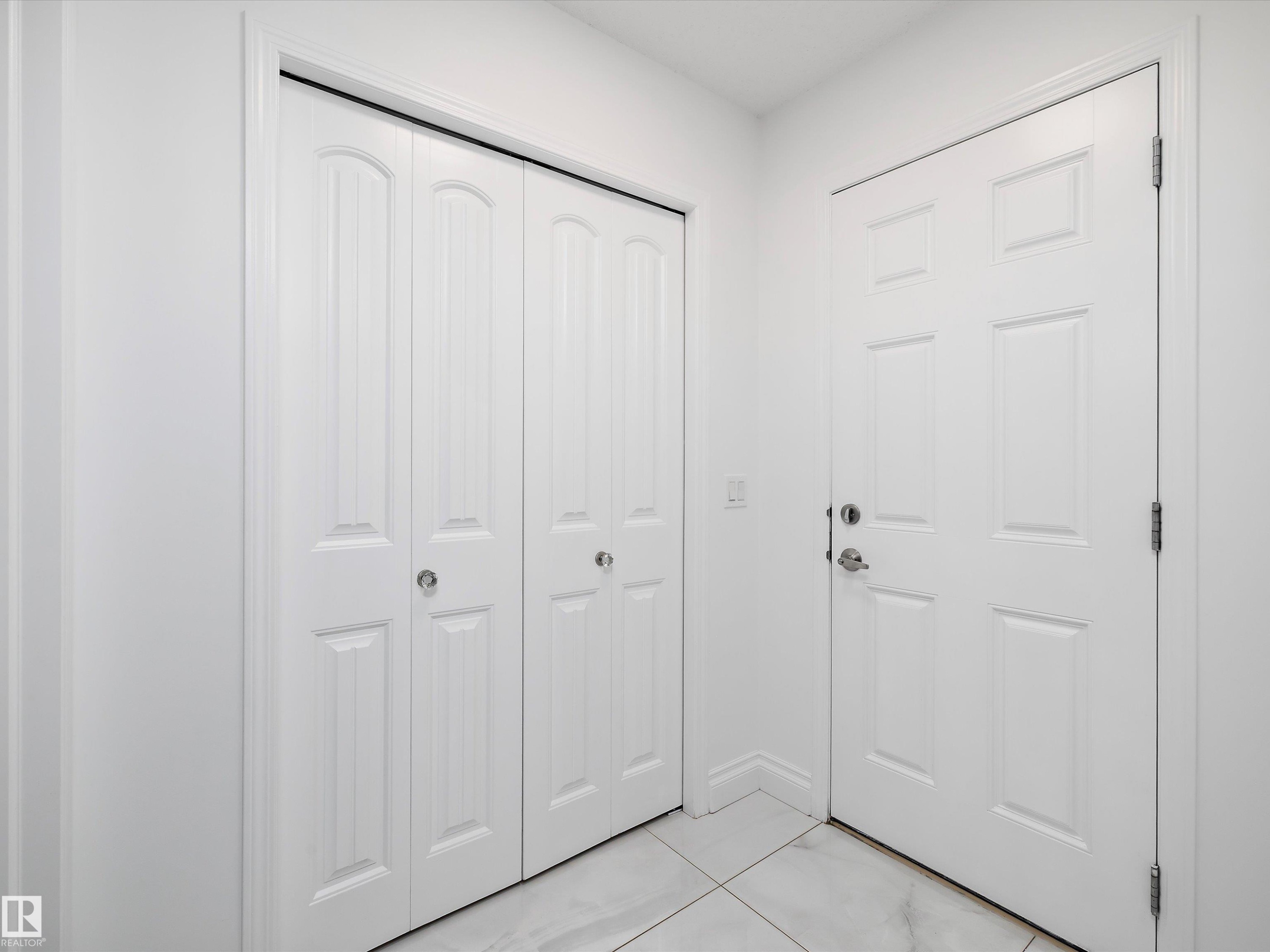 Entryway featuring a white paneled door and bifold closet doors, complemented by white tile flooring - 9852 217 Street, Edmonton, AB - Indoor Photo Showing Other Room