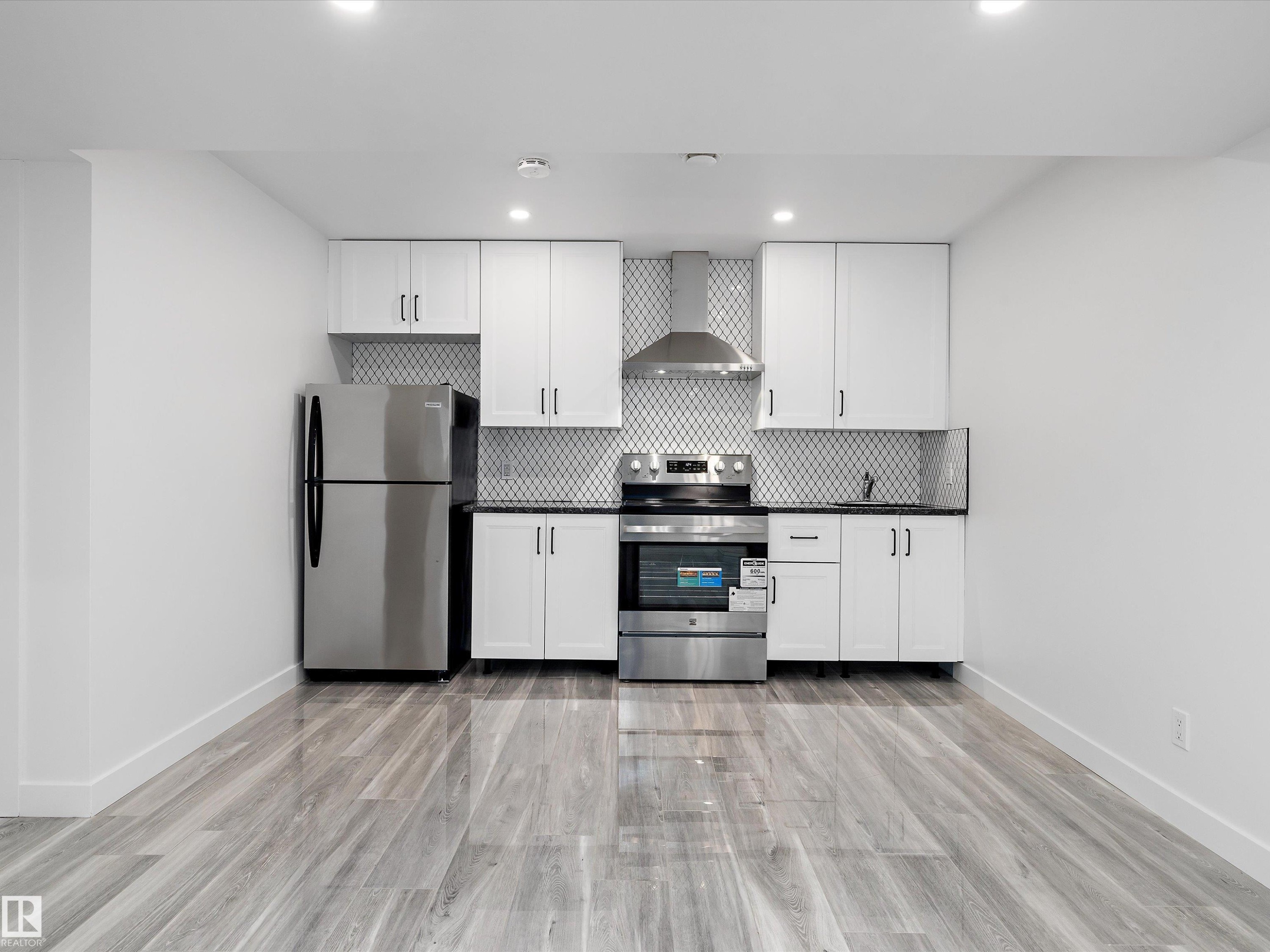 The kitchen features stainless steel appliances, white cabinetry, and a patterned tile backsplash - 9852 217 Street, Edmonton, AB - Indoor Photo Showing Kitchen
