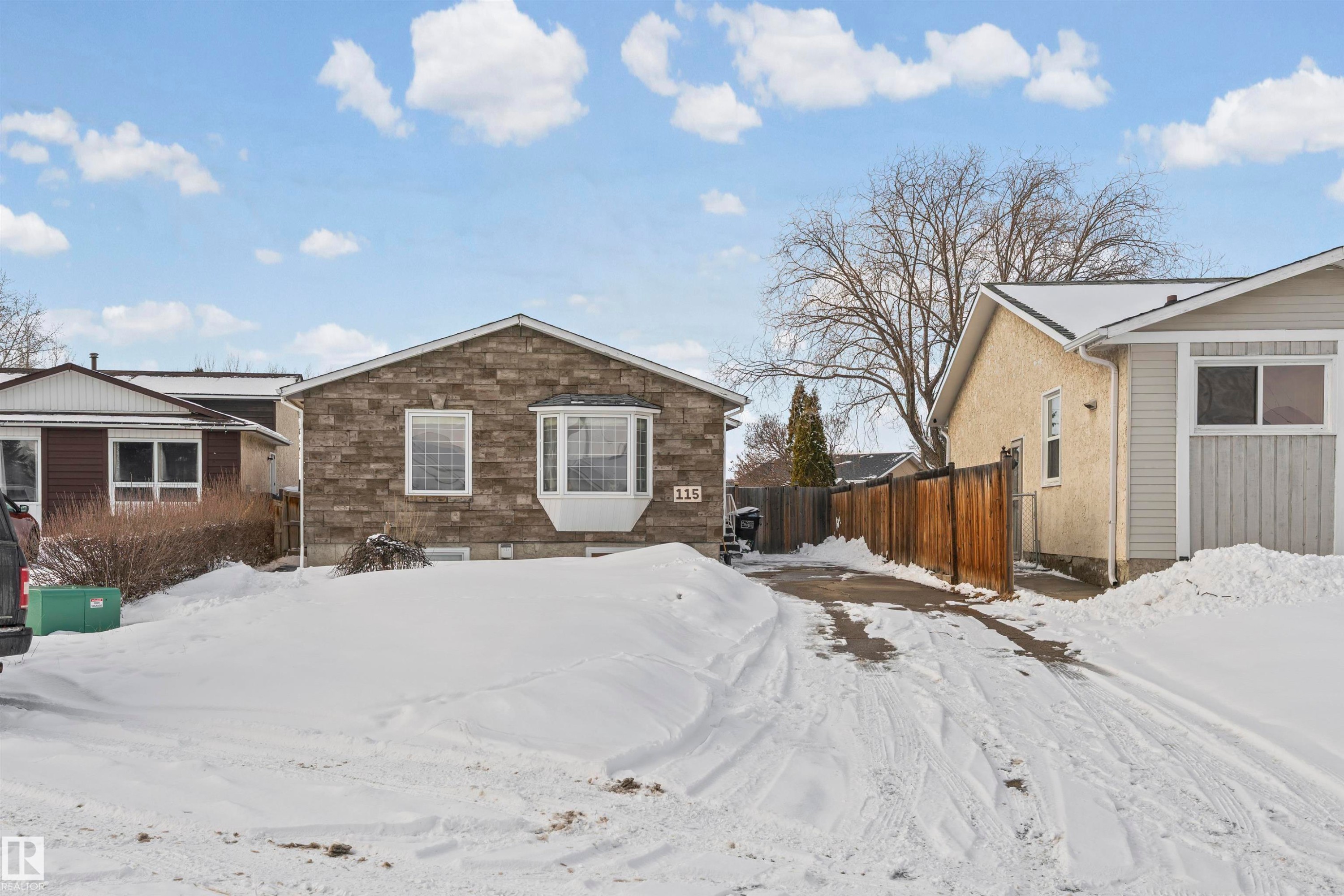 Stone facade home featuring a prominent bay window, white window trim, and a paved driveway - 115 Warwick Road, Edmonton, AB - Outdoor
