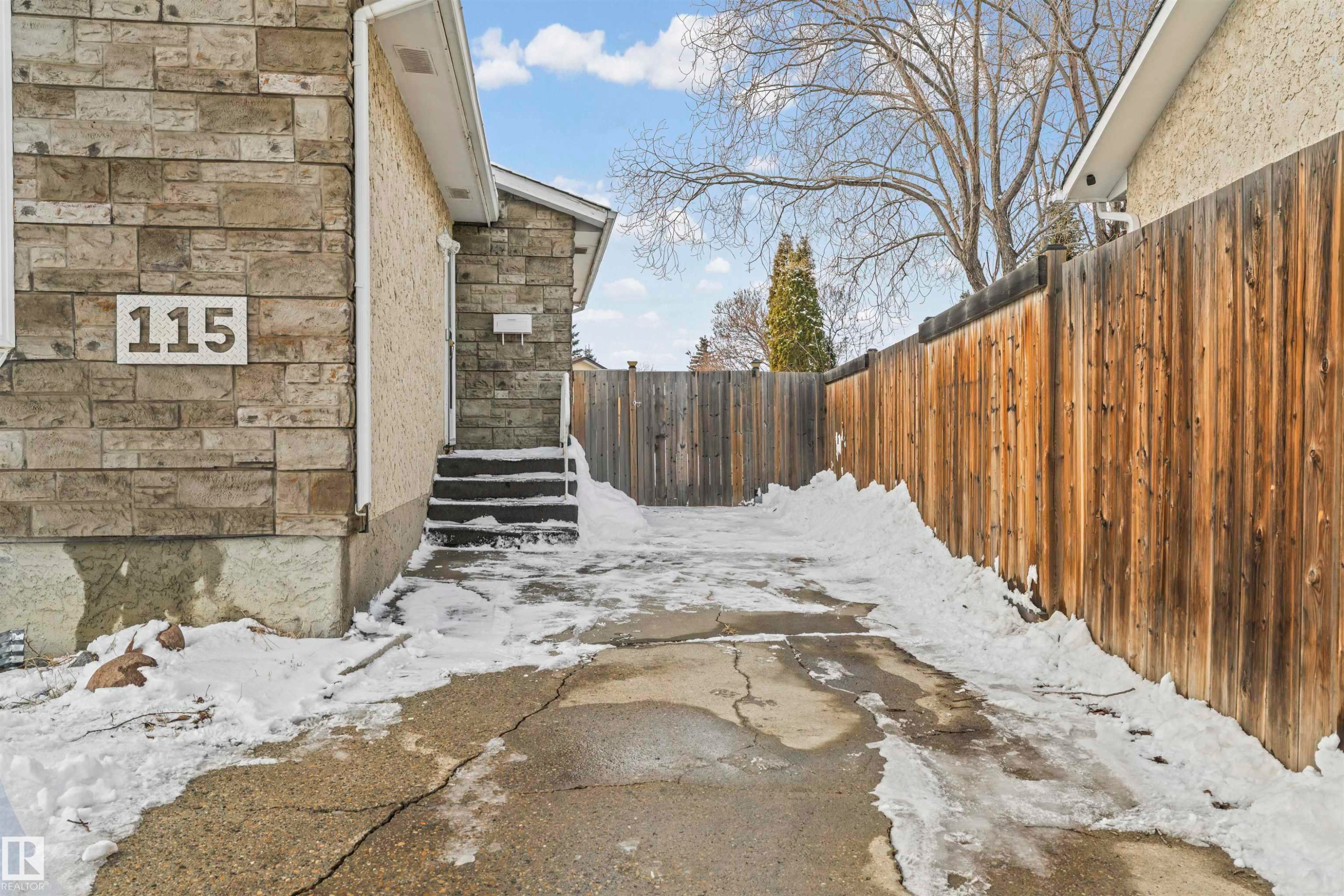 Exterior featuring stone and stucco finishes, a paved driveway, and a wood privacy fence - 115 Warwick Road, Edmonton, AB - Outdoor