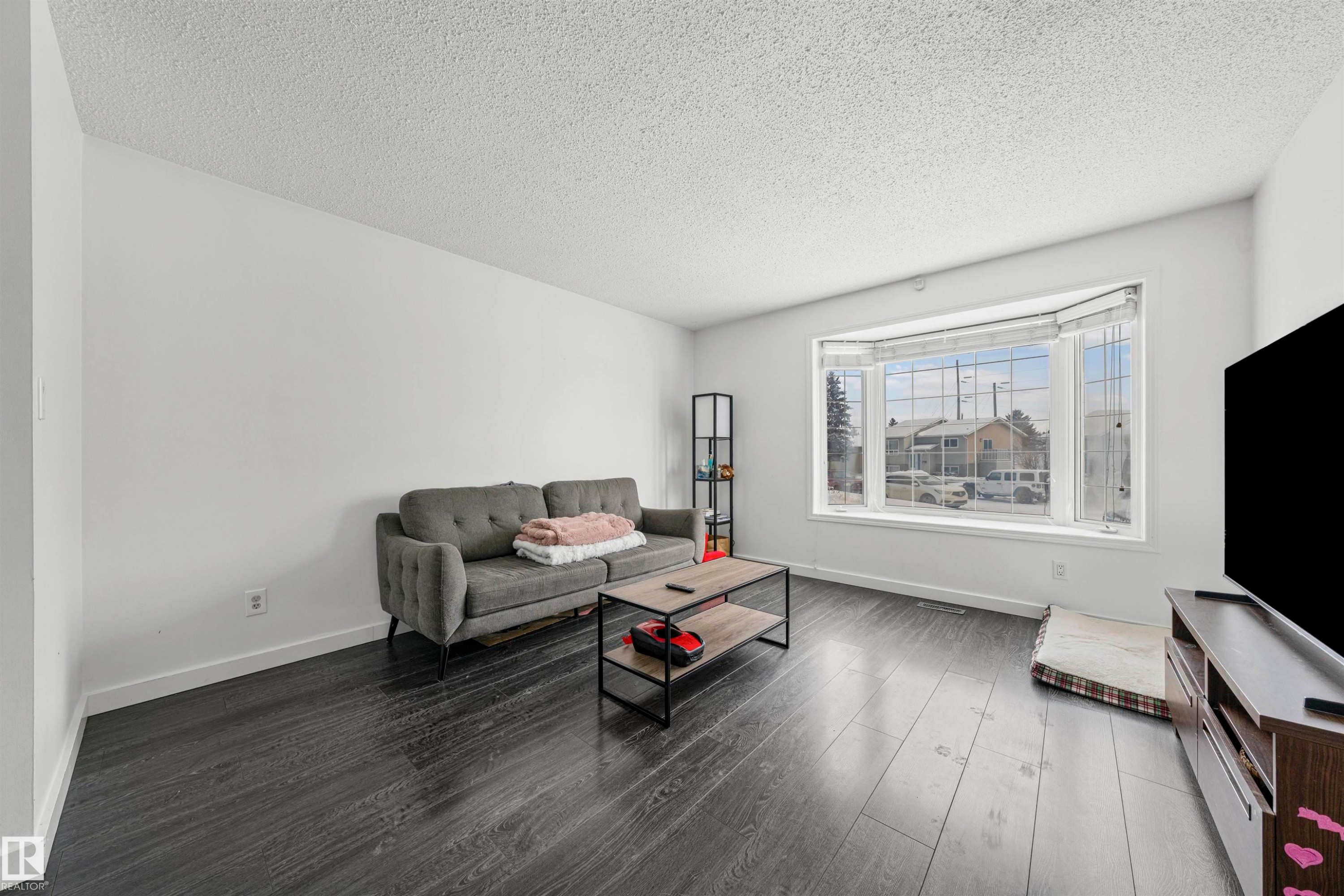 Spacious living area featuring dark wood-finish flooring, white walls, and a large bay window - 115 Warwick Road, Edmonton, AB - Indoor Photo Showing Living Room