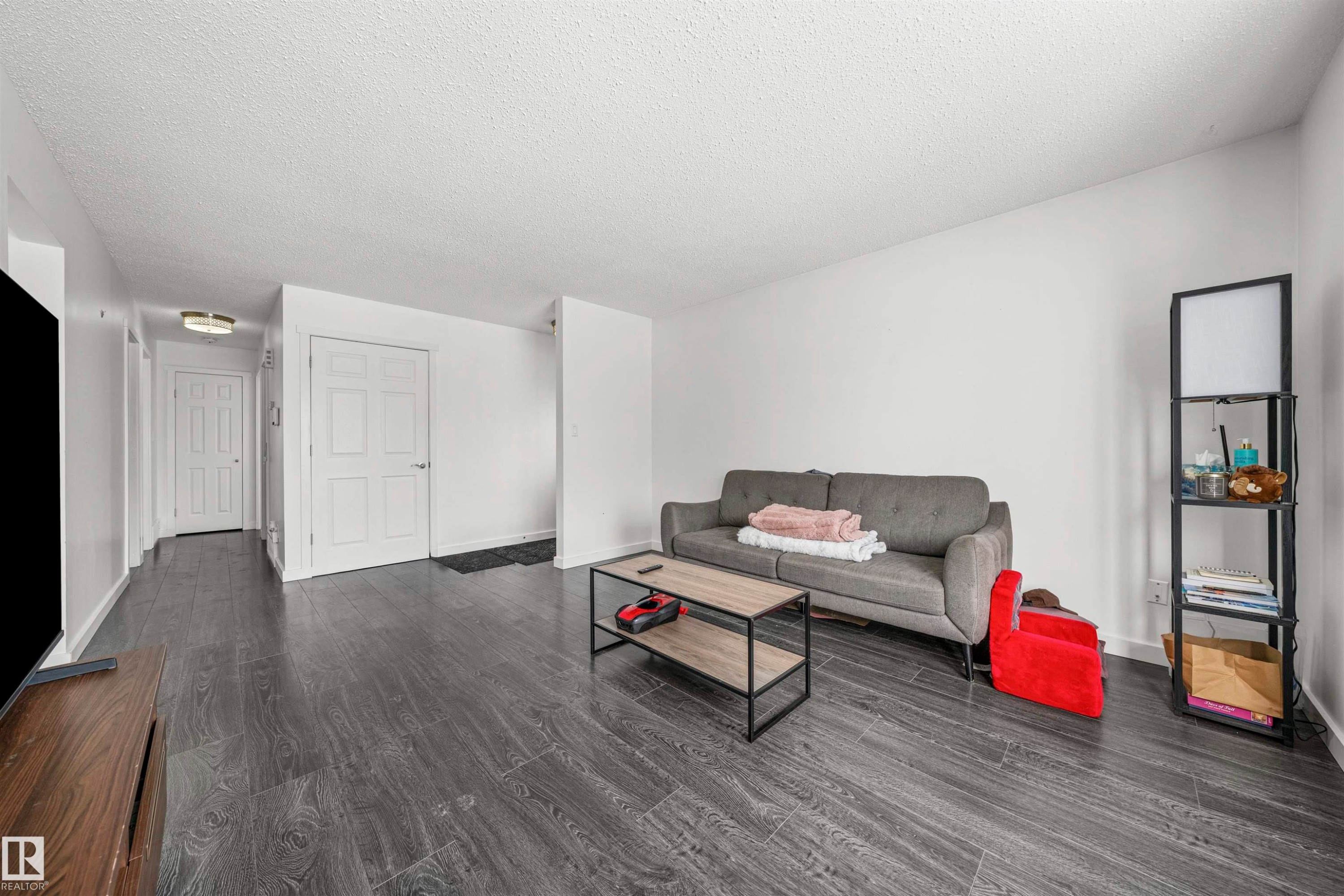 Spacious living area featuring dark wood-finish flooring, white painted walls, and a textured white ceiling - 115 Warwick Road, Edmonton, AB - Indoor