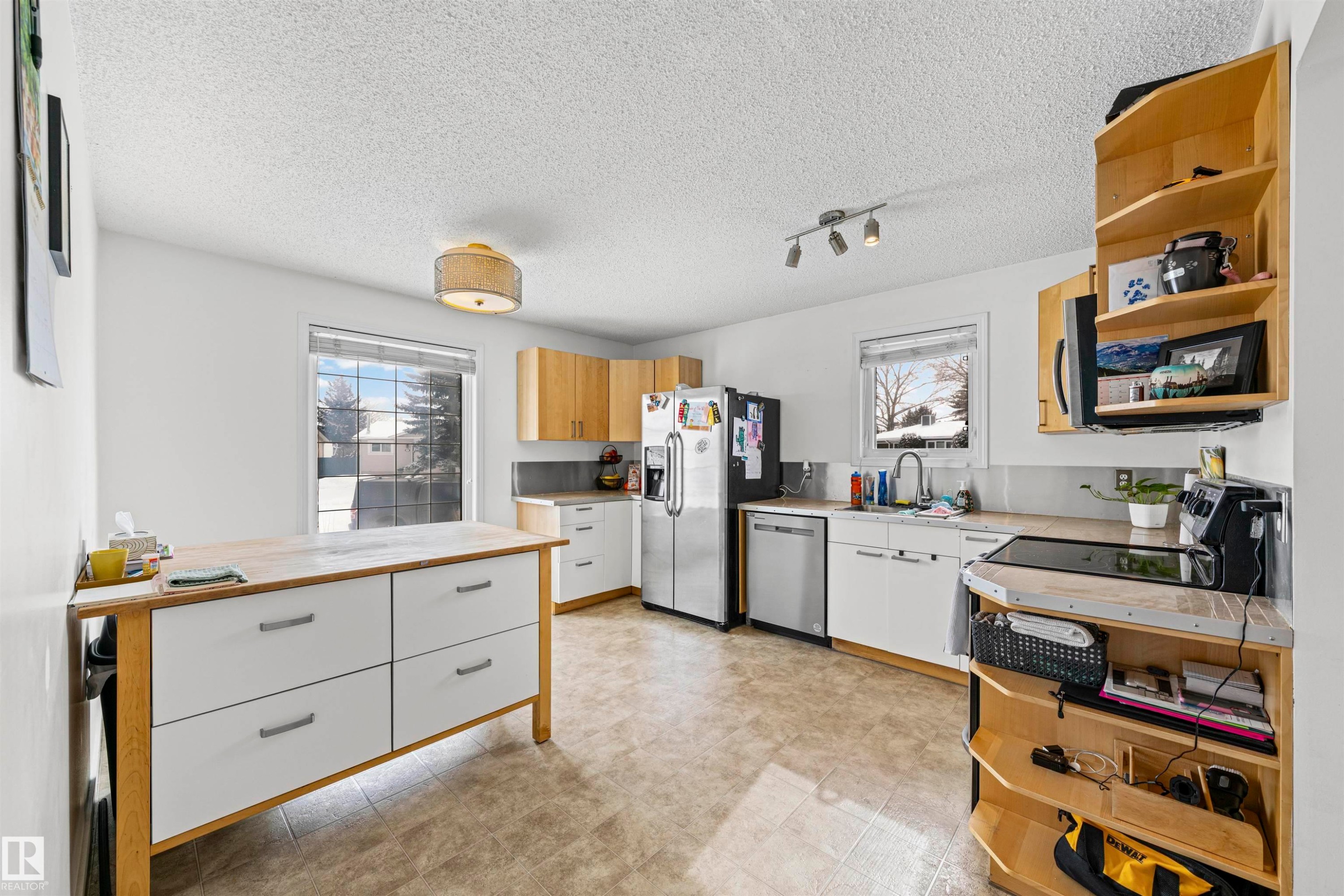 Kitchen featuring stainless steel appliances, wood-finish cabinetry, a central island with white drawers, and tile flooring - 115 Warwick Road, Edmonton, AB - Indoor Photo Showing Kitchen