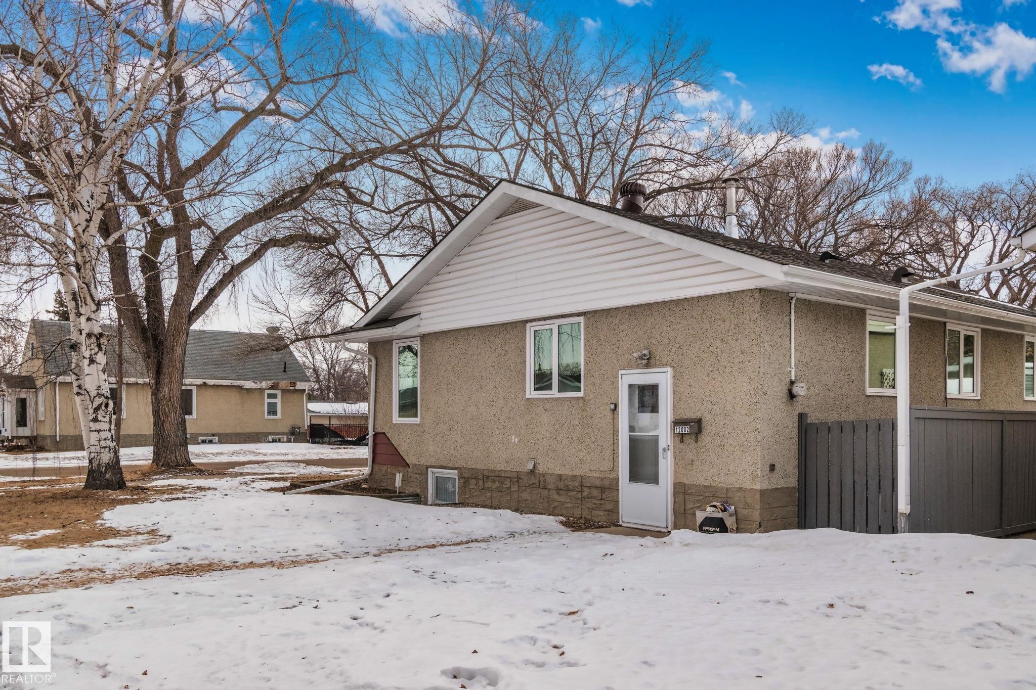 Residence featuring a stucco exterior with a stone-finish foundation, white trim, and a gabled roof - 12002 37 Street, Edmonton, AB - Outdoor