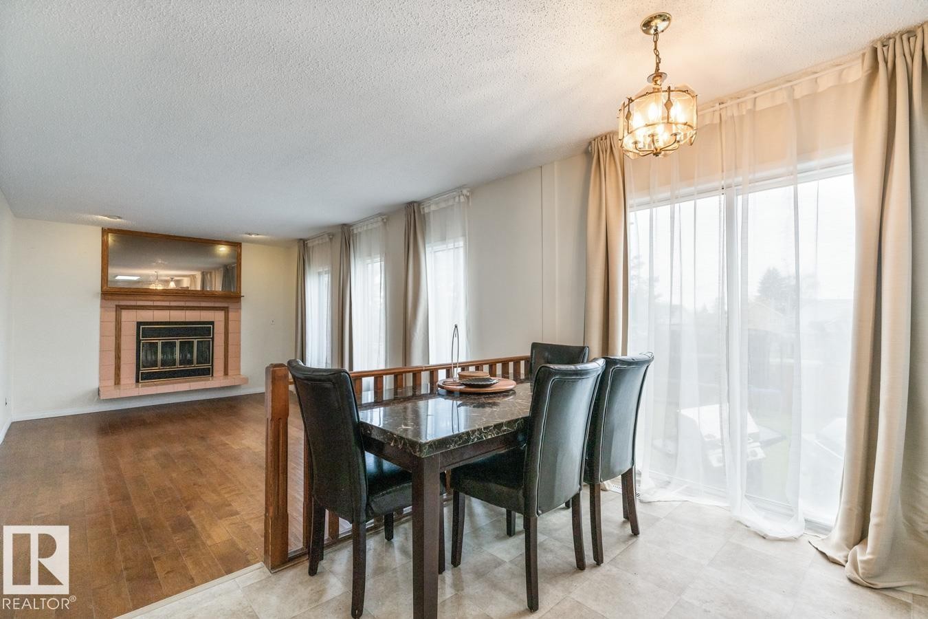 Dining area featuring a contemporary chandelier, tile flooring, and sliding glass doors with sheer and blackout curtains - 4340 33 Street, Edmonton, AB - Indoor Photo Showing Dining Room With Fireplace