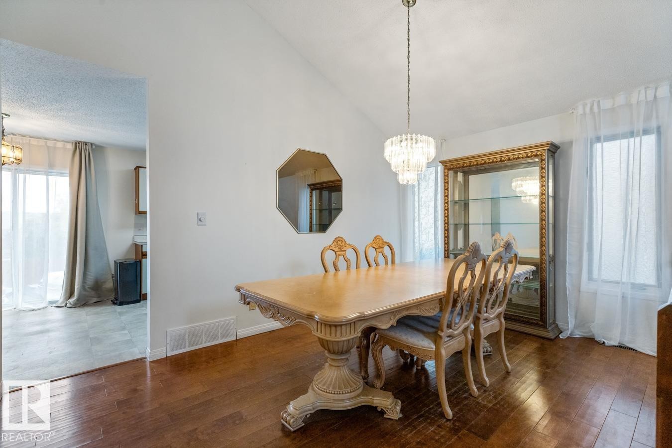 Vaulted ceiling formal dining space featuring wood-finish flooring, a tiered crystal chandelier, and a large window - 4340 33 Street, Edmonton, AB - Indoor Photo Showing Dining Room