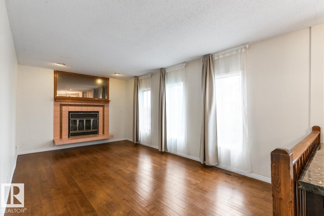 Living space featuring wood-finish flooring, a tiled fireplace with a metal insert, a wood mantel, and an integrated mirrored accent - 4340 33 Street, Edmonton, AB - Indoor Photo Showing Living Room With Fireplace