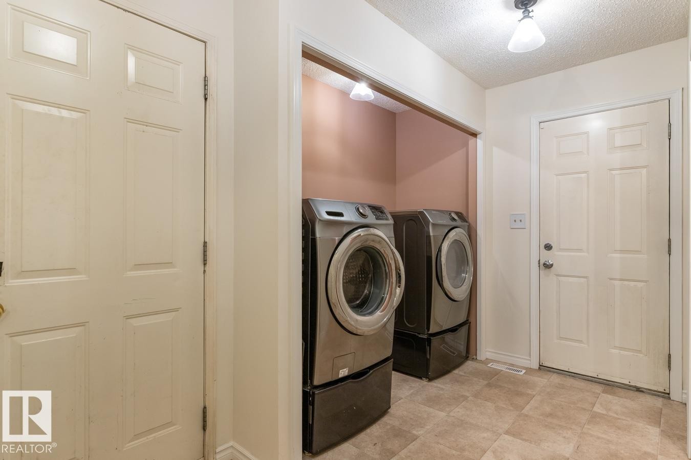 Dedicated laundry area featuring front-loading machines on pedestals, tile flooring, and integrated lighting - 4340 33 Street, Edmonton, AB - Indoor Photo Showing Laundry Room