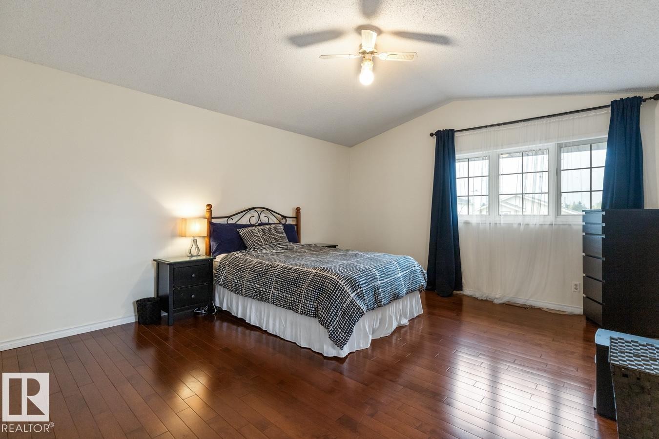 Vaulted ceiling with an attached ceiling fan, hardwood flooring, and a large window with white muntins - 4340 33 Street, Edmonton, AB - Indoor Photo Showing Bedroom