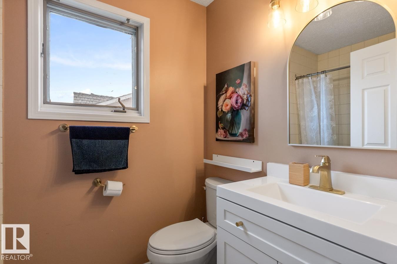 Bathroom featuring a white vanity with integrated sink, brass-finish faucet, and coordinating arched mirror - 4340 33 Street, Edmonton, AB - Indoor Photo Showing Bathroom