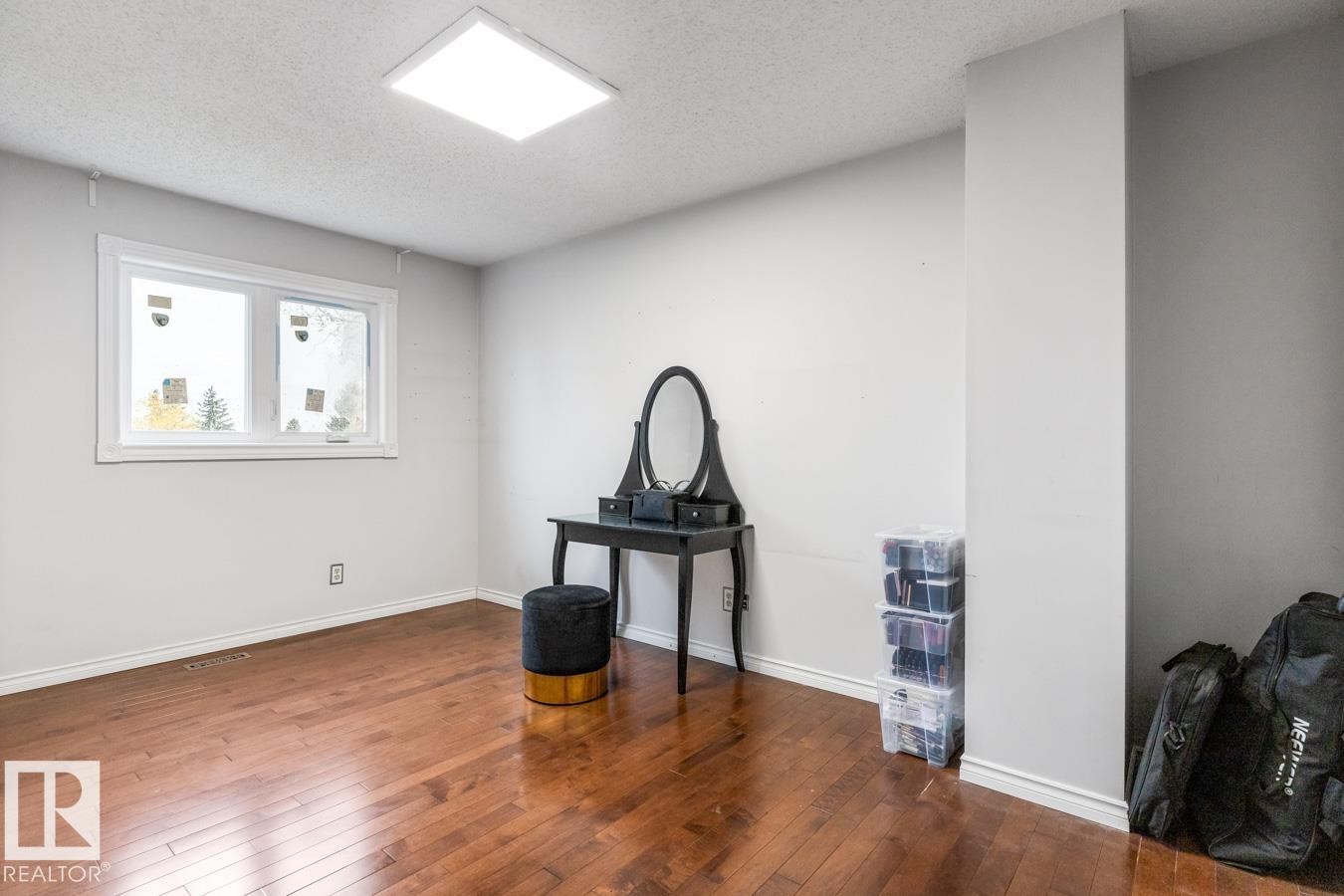 Spacious room featuring wood-finish flooring, a large window with white trim, light gray painted walls, and a rectangular ceiling light fixture - 4340 33 Street, Edmonton, AB - Indoor Photo Showing Other Room