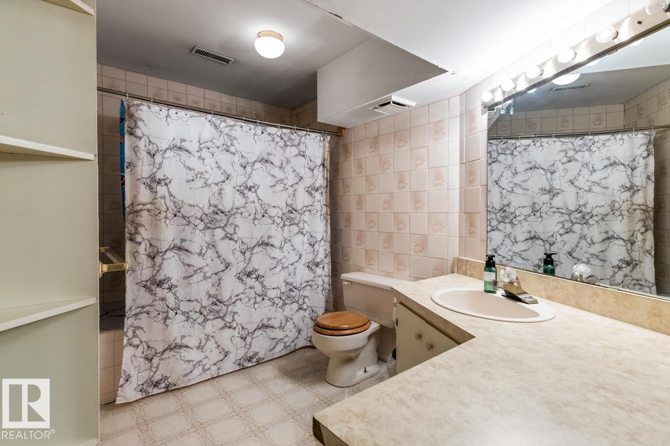 Bathroom featuring a vanity with an integrated sink, a built-in toilet, a shower area with a curtain rod, built-in shelving, and a large wall-mounted mirror with overhead lighting - 4340 33 Street, Edmonton, AB - Indoor Photo Showing Bathroom