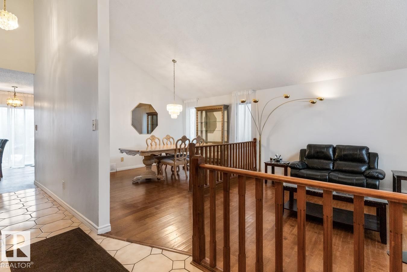 Entryway with geometric tile flooring opening into a living space featuring wood flooring, a vaulted ceiling, and a wooden banister - 4340 33 Street, Edmonton, AB - Indoor