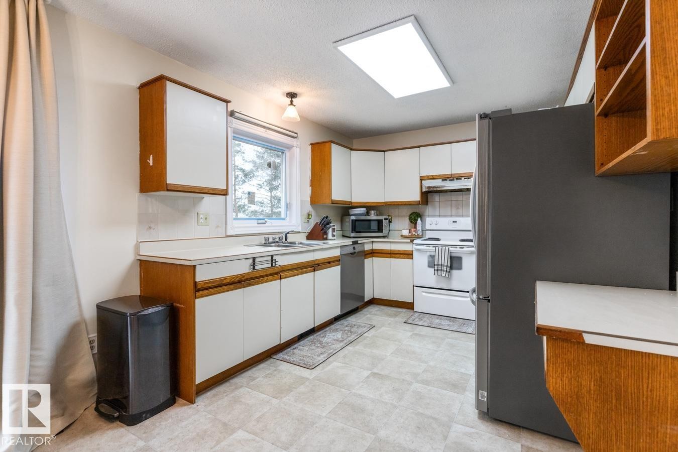 Kitchen featuring white cabinetry with wood-finish trim, a stainless steel dishwasher, and a white electric range with a built-in microwave above - 4340 33 Street, Edmonton, AB - Indoor Photo Showing Kitchen