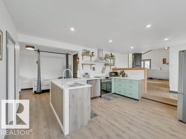 Modern kitchen featuring a central island with an undermount sink, light wood-finish flooring, recessed lighting, stainless steel appliances, and mint green base cabinetry - 3602 50Th Ave, Sylvan Lake, AB - Indoor Photo Showing Other Room