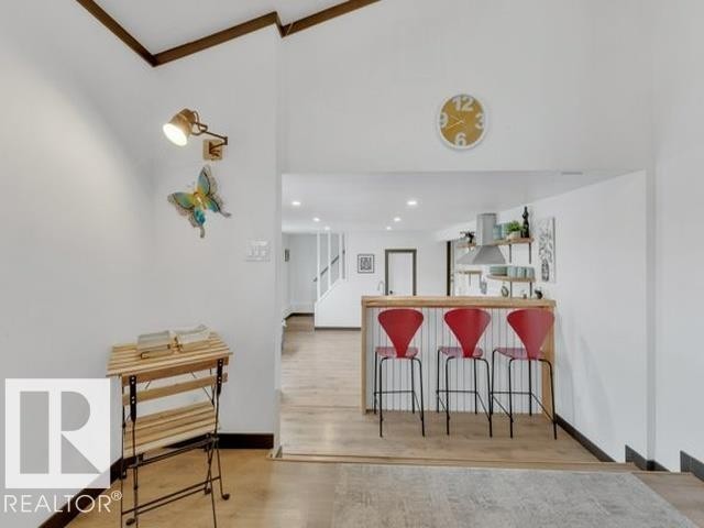 Open-concept interior featuring wood-finish flooring, a breakfast bar with beadboard paneling, and a contemporary wall-mounted light fixture - 3602 50Th Ave, Sylvan Lake, AB - Indoor Photo Showing Other Room