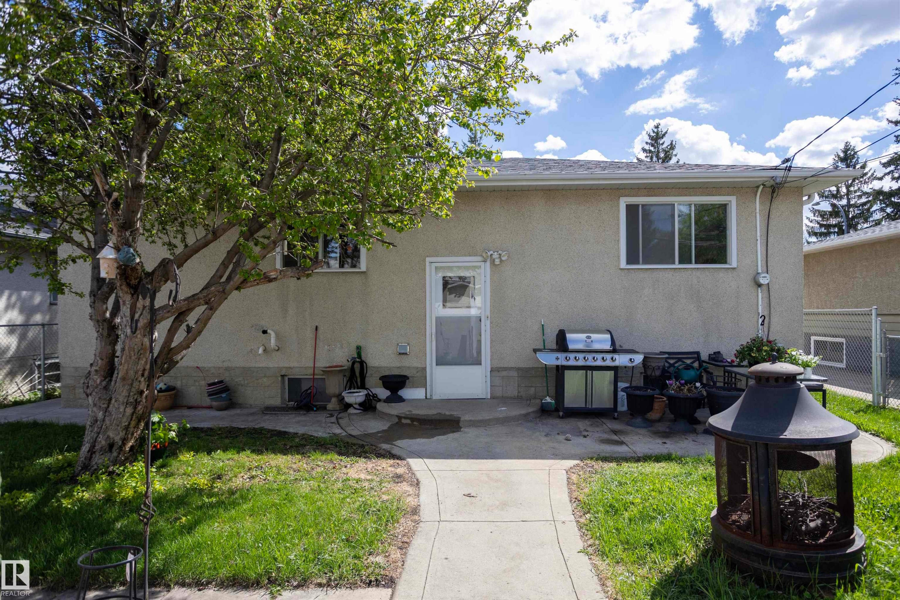 Rear exterior with a concrete patio, mature tree, and a concrete pathway - 10428 68 Avenue, Edmonton, AB - Outdoor
