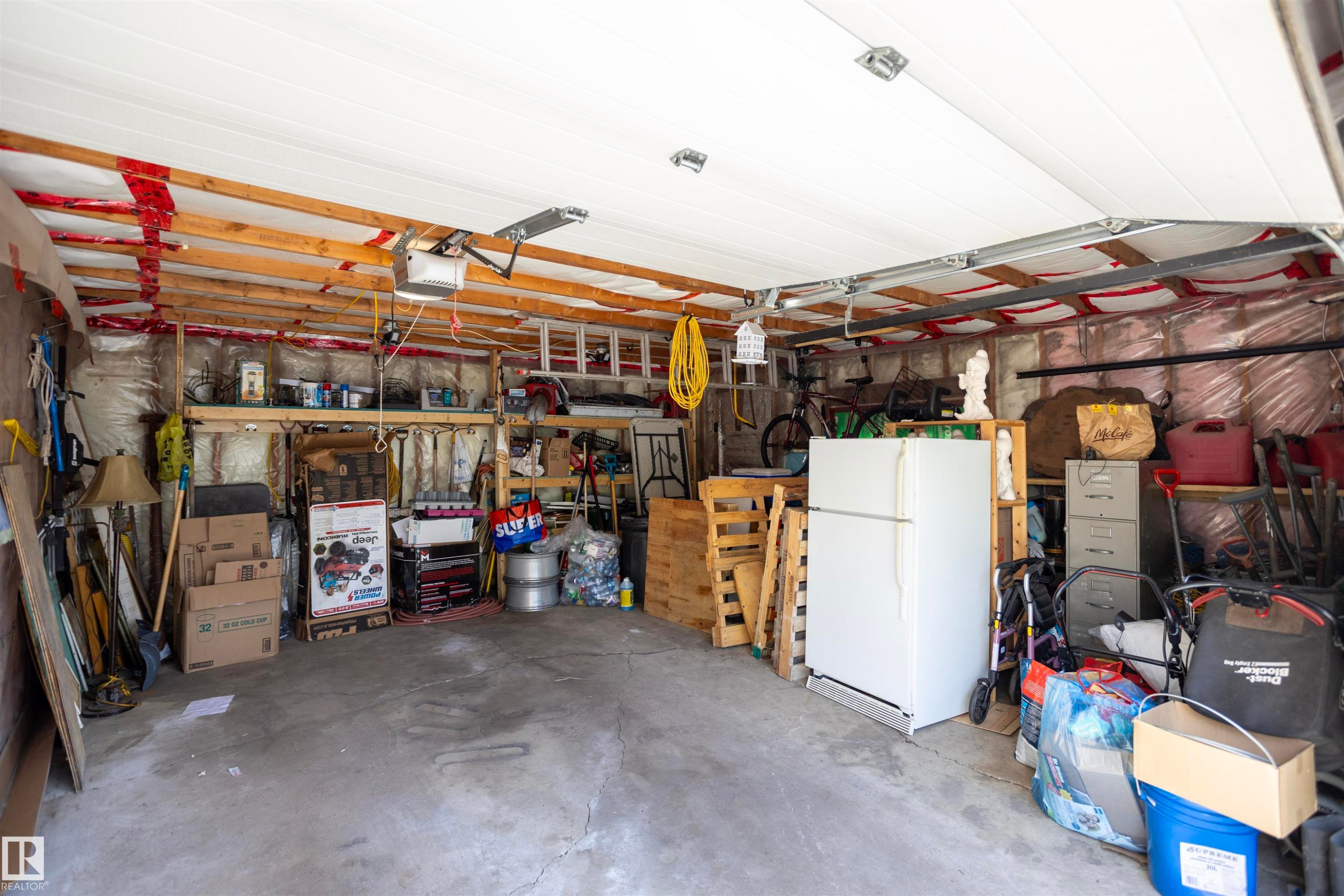 Spacious garage featuring a concrete floor, exposed wooden ceiling beams, and a white overhead garage door - 10428 68 Avenue, Edmonton, AB - Indoor Photo Showing Garage