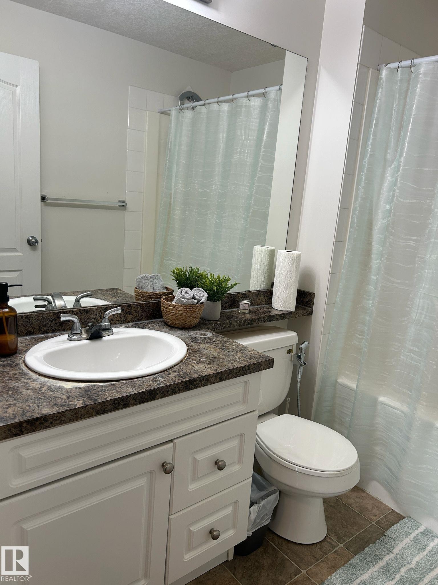 Bathroom featuring a white vanity with panel cabinetry and satin nickel hardware, a dark speckled countertop, an integrated sink, and a full-width mirror - 1228 9363 Simpson Drive, Edmonton, AB - Indoor Photo Showing Bathroom