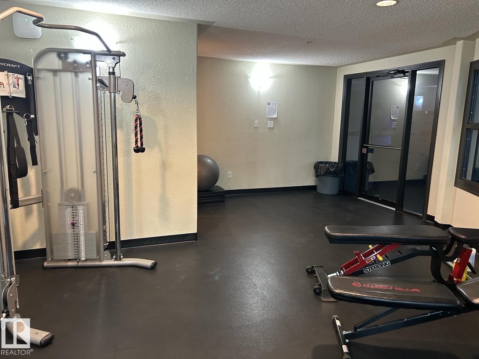 Dedicated fitness space featuring rubber flooring, a cable weight machine, and an adjustable utility bench - 1228 9363 Simpson Drive, Edmonton, AB - Indoor Photo Showing Gym Room