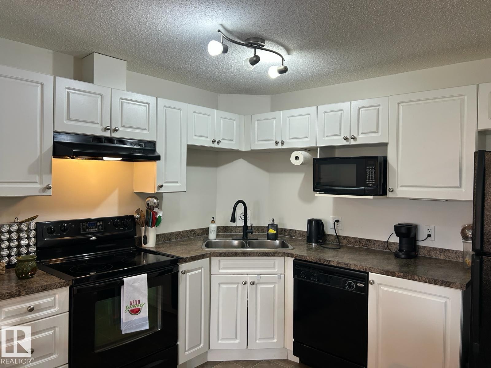 Kitchen featuring white cabinetry with brushed nickel hardware, dark countertops, a built-in oven with an electric cooktop, a mounted microwave, and a black dishwasher - 1228 9363 Simpson Drive, Edmonton, AB - Indoor Photo Showing Kitchen With Double Sink