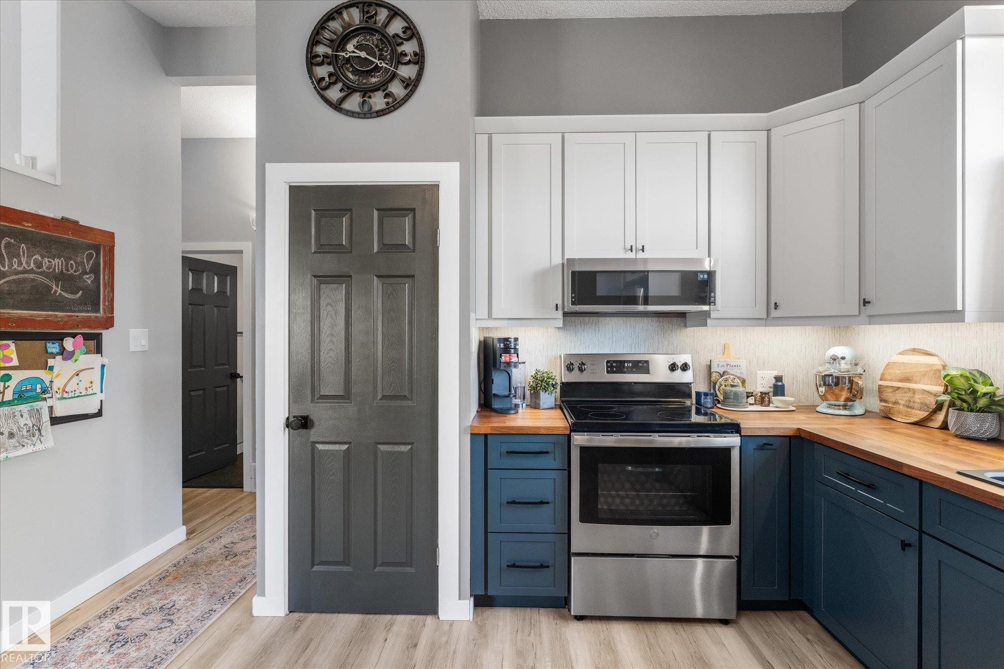 Modern kitchen featuring two-tone cabinetry with light upper cabinets and contrasting dark lower cabinets, butcher block countertops, and stainless steel appliances including a range and microwave - 4759 48 Street, Onoway, AB - Indoor Photo Showing Kitchen