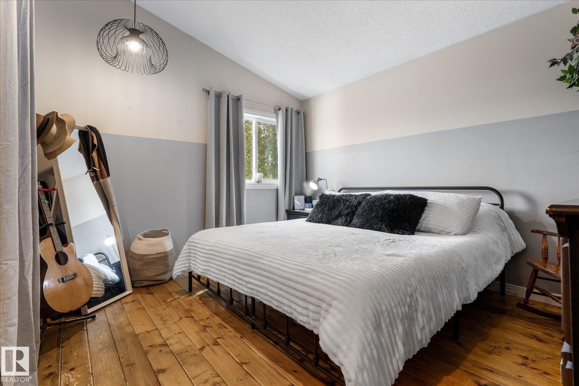 Bedroom featuring wood-finish flooring, a window with grey curtains, and a two-tone painted wall - 4759 48 Street, Onoway, AB - Indoor Photo Showing Bedroom