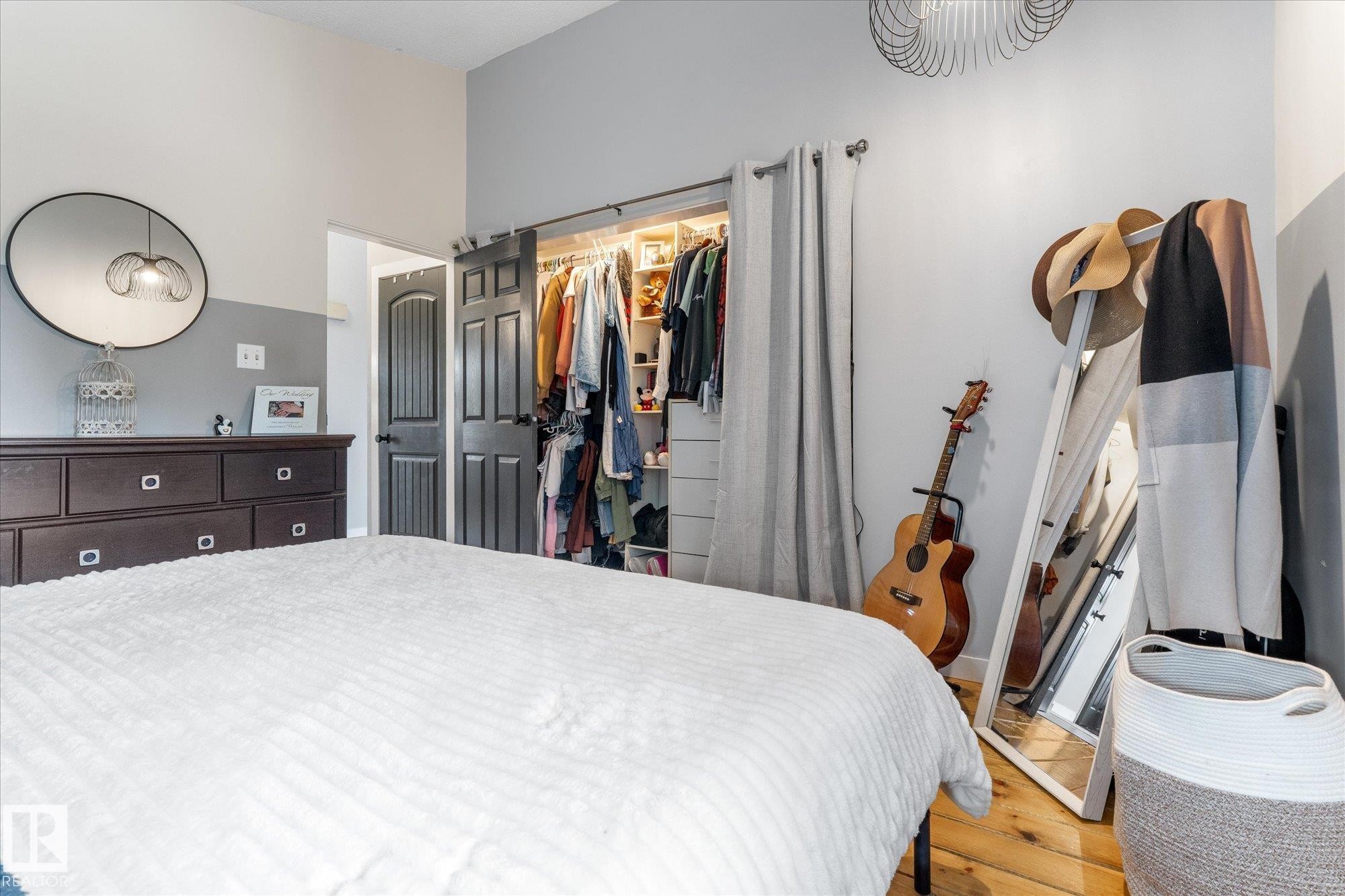 Bedroom featuring a closet with sliding barn doors, natural wood-finish flooring, and a contemporary light fixture - 4759 48 Street, Onoway, AB - Indoor Photo Showing Bedroom