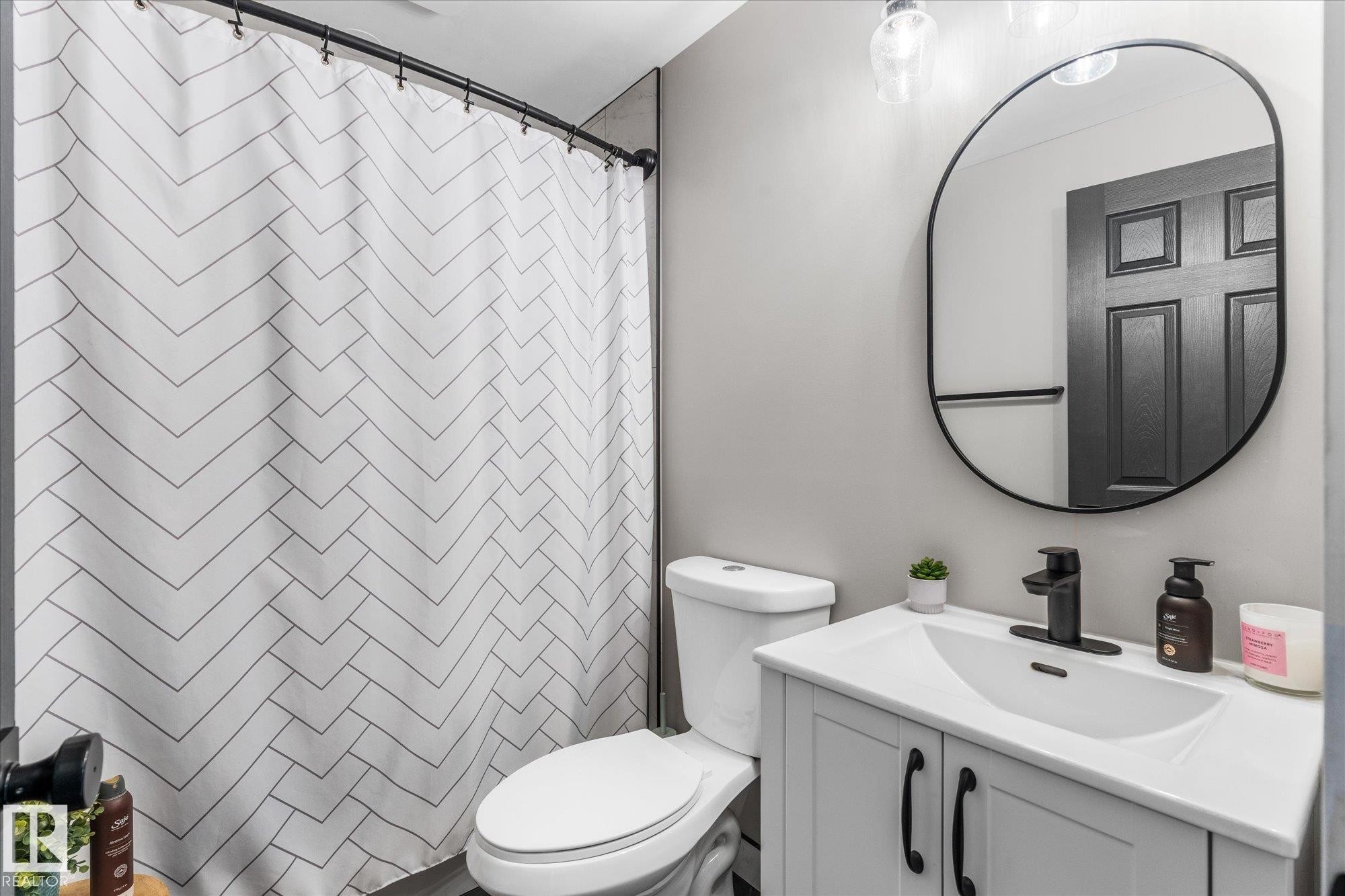 Bathroom featuring a white vanity with black hardware, a black framed oval mirror, and a white toilet - 4759 48 Street, Onoway, AB - Indoor Photo Showing Bathroom