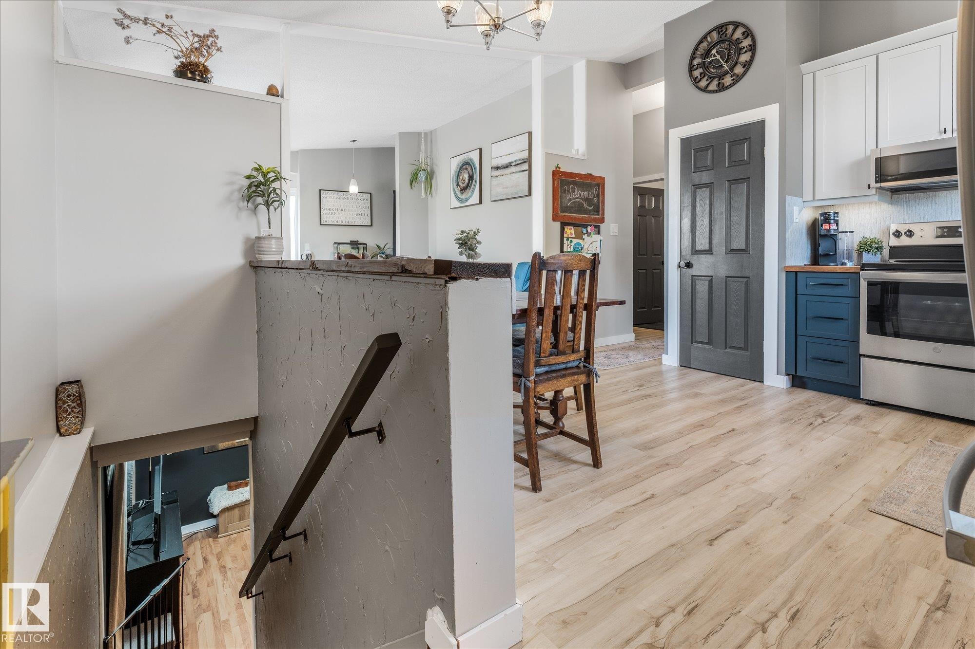 Open-concept kitchen and dining area featuring light wood-finish flooring, white upper cabinetry, blue lower cabinetry, stainless steel appliances, and a dark paneled door with white trim - 4759 48 Street, Onoway, AB - Indoor Photo Showing Kitchen