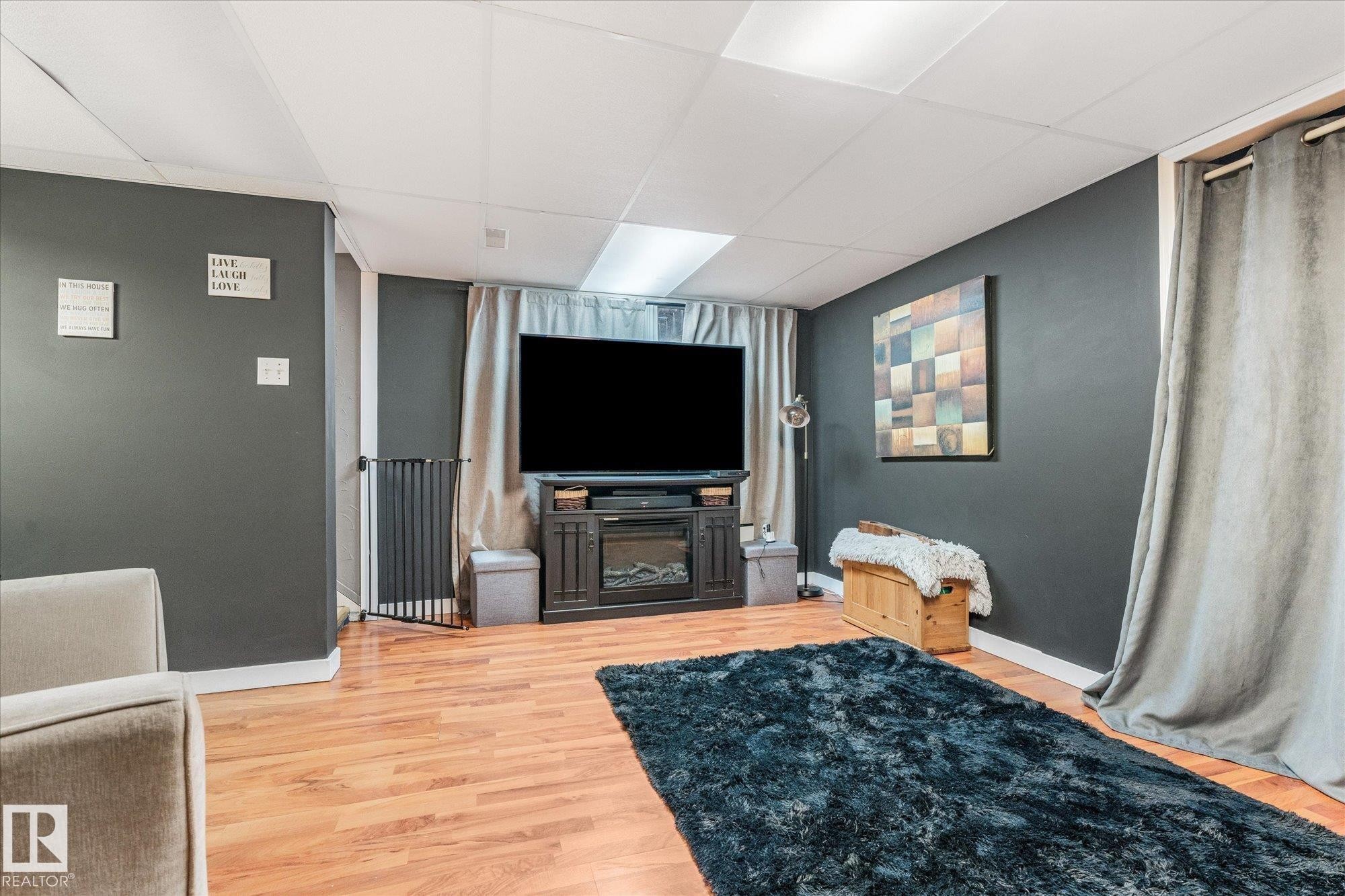 Spacious room featuring wood-finish flooring, dark accent walls, and a dropped ceiling with integrated lighting - 4759 48 Street, Onoway, AB - Indoor