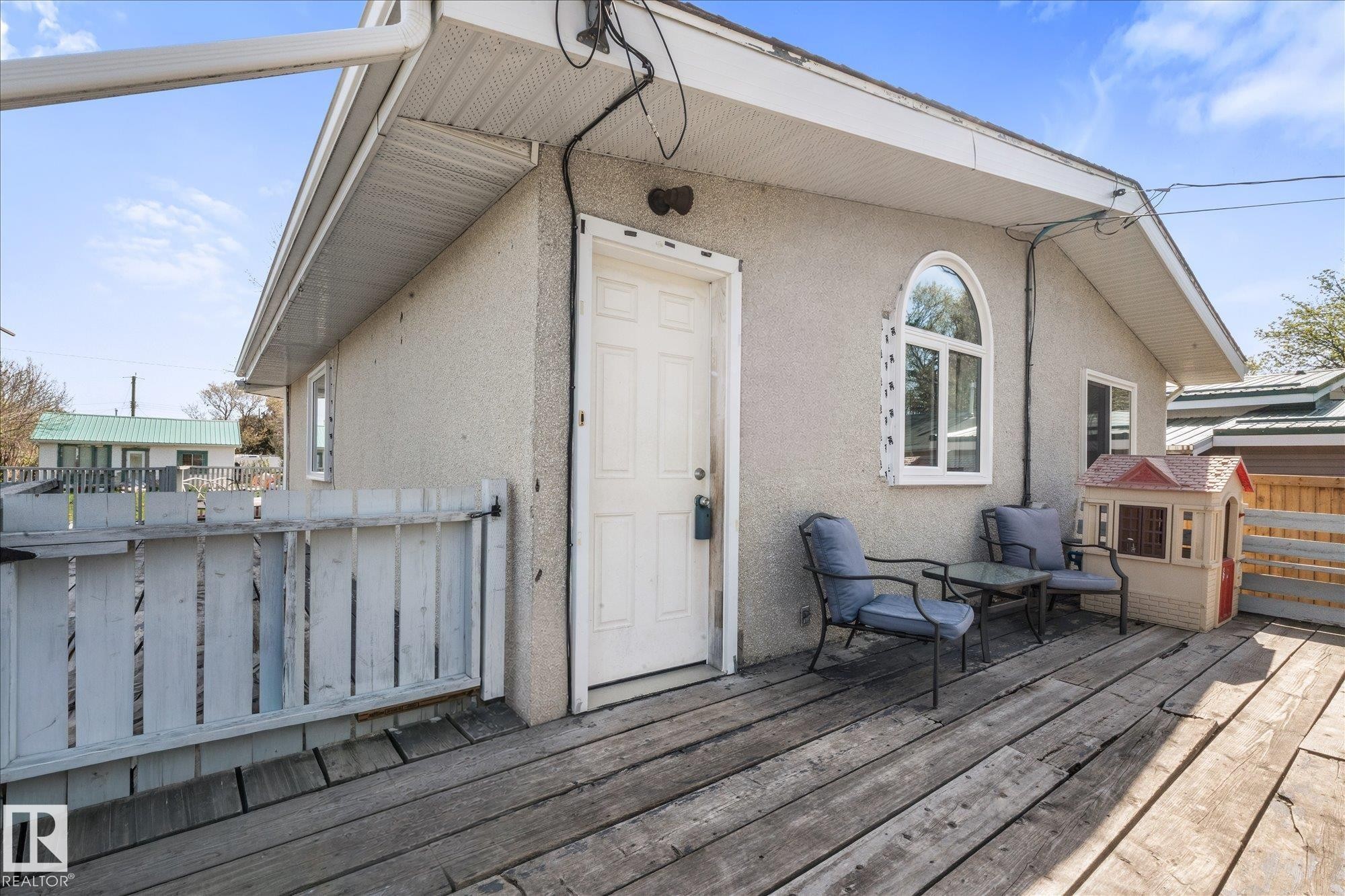 Exterior deck space featuring a textured stucco finish, a white entry door, and an arched window - 4759 48 Street, Onoway, AB - Outdoor With Deck Patio Veranda With Exterior