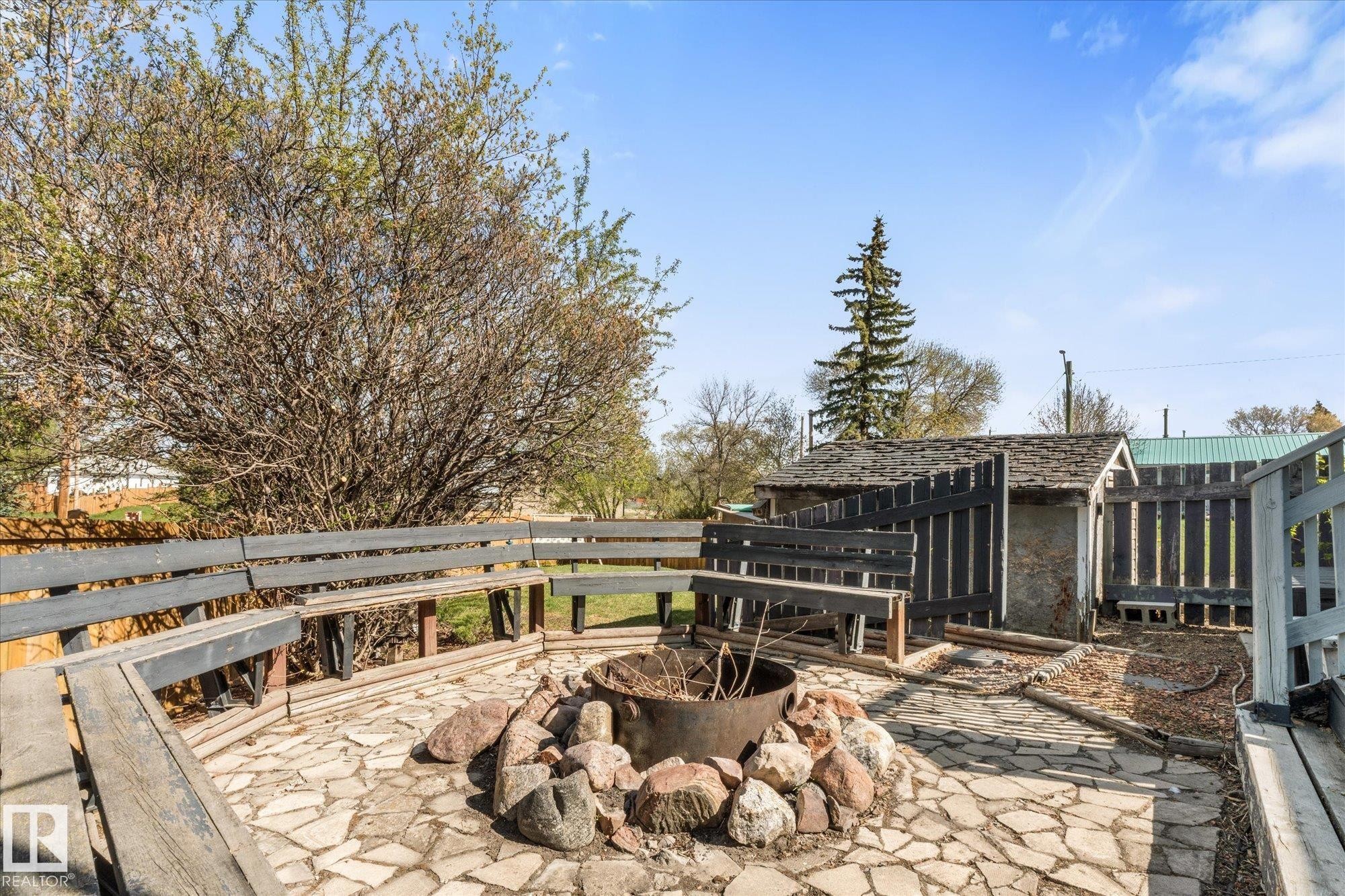 Stone patio featuring a central fire pit surrounded by a built-in wooden bench - 4759 48 Street, Onoway, AB - Outdoor With Deck Patio Veranda