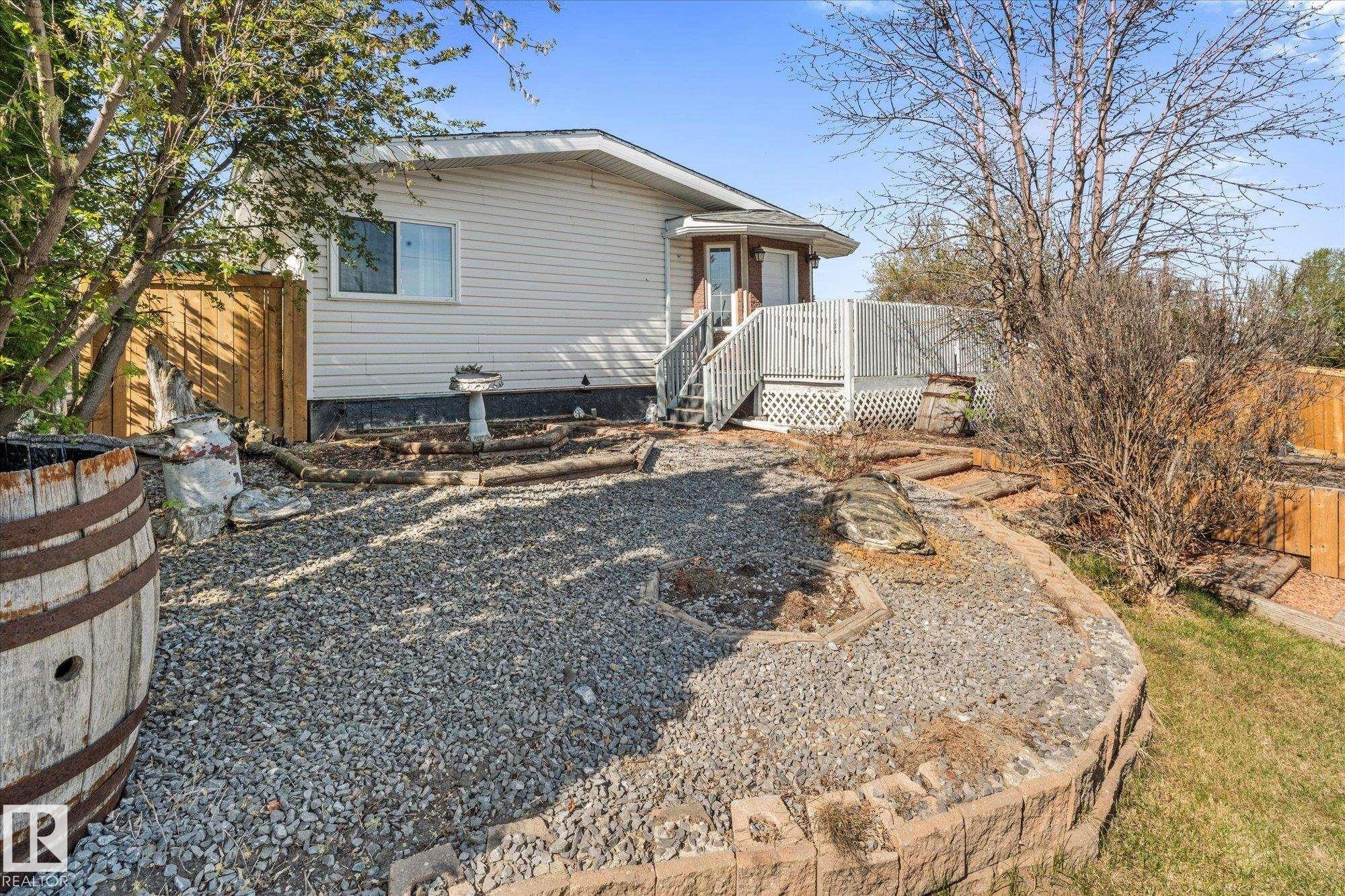 Rear exterior featuring white vinyl siding, a multi-level deck with white railing, and a gravel patio area - 4759 48 Street, Onoway, AB - Outdoor