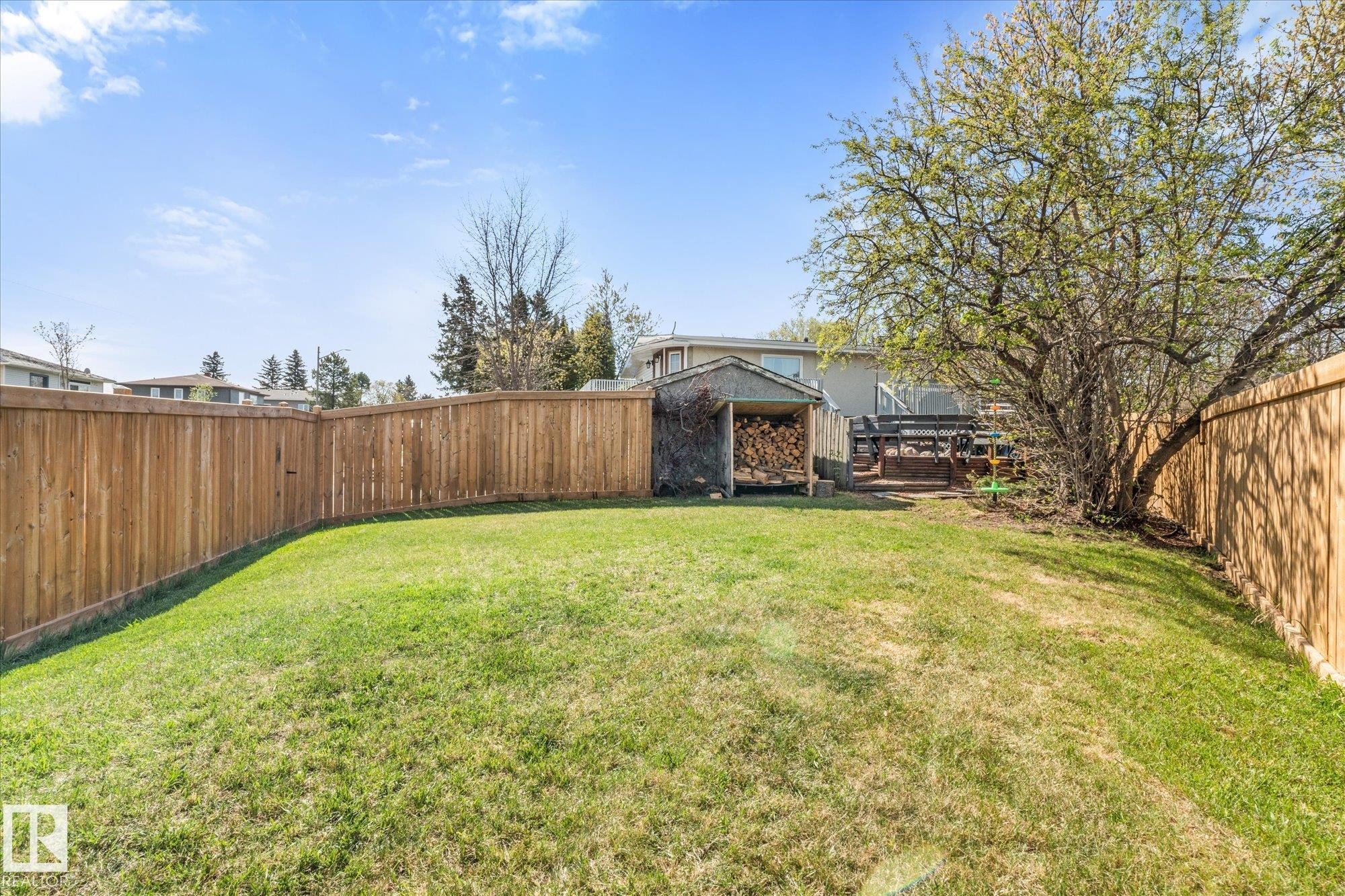 Expansive fenced yard featuring a spacious lawn, a mature deciduous tree, a wood-sided shed, and a raised wood deck - 4759 48 Street, Onoway, AB - Outdoor