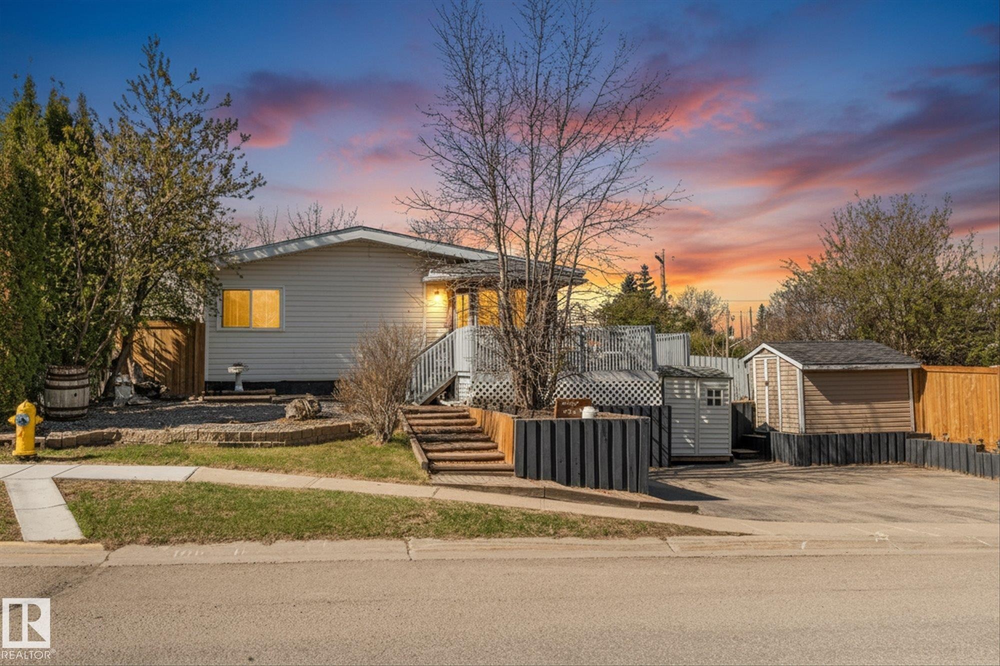 Single-story residence featuring light gray siding, a multi-level deck with white lattice accents, and exterior lighting - 4759 48 Street, Onoway, AB - Outdoor