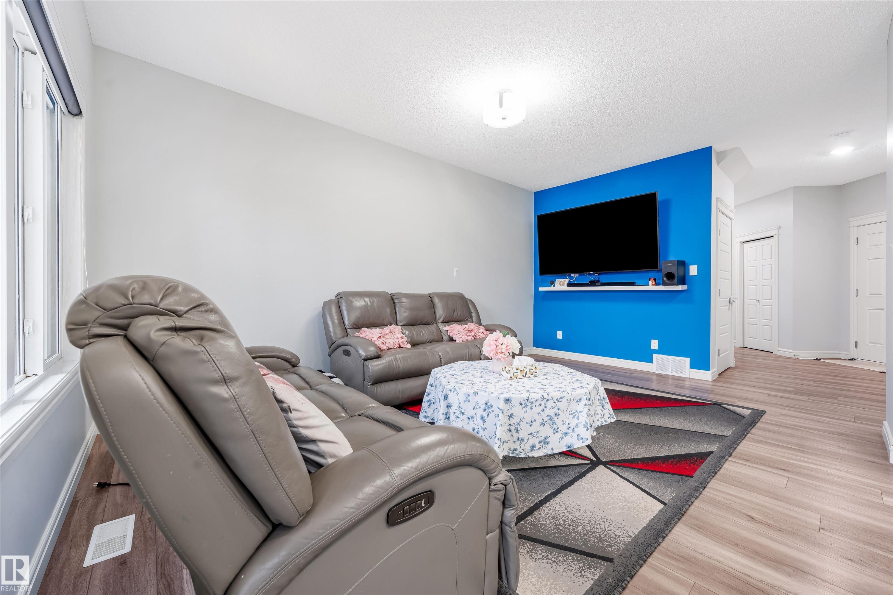Bright living area featuring a prominent accent wall with a wall-mounted television and a floating shelf - 1024 Daniels Loop, Edmonton, AB - Indoor