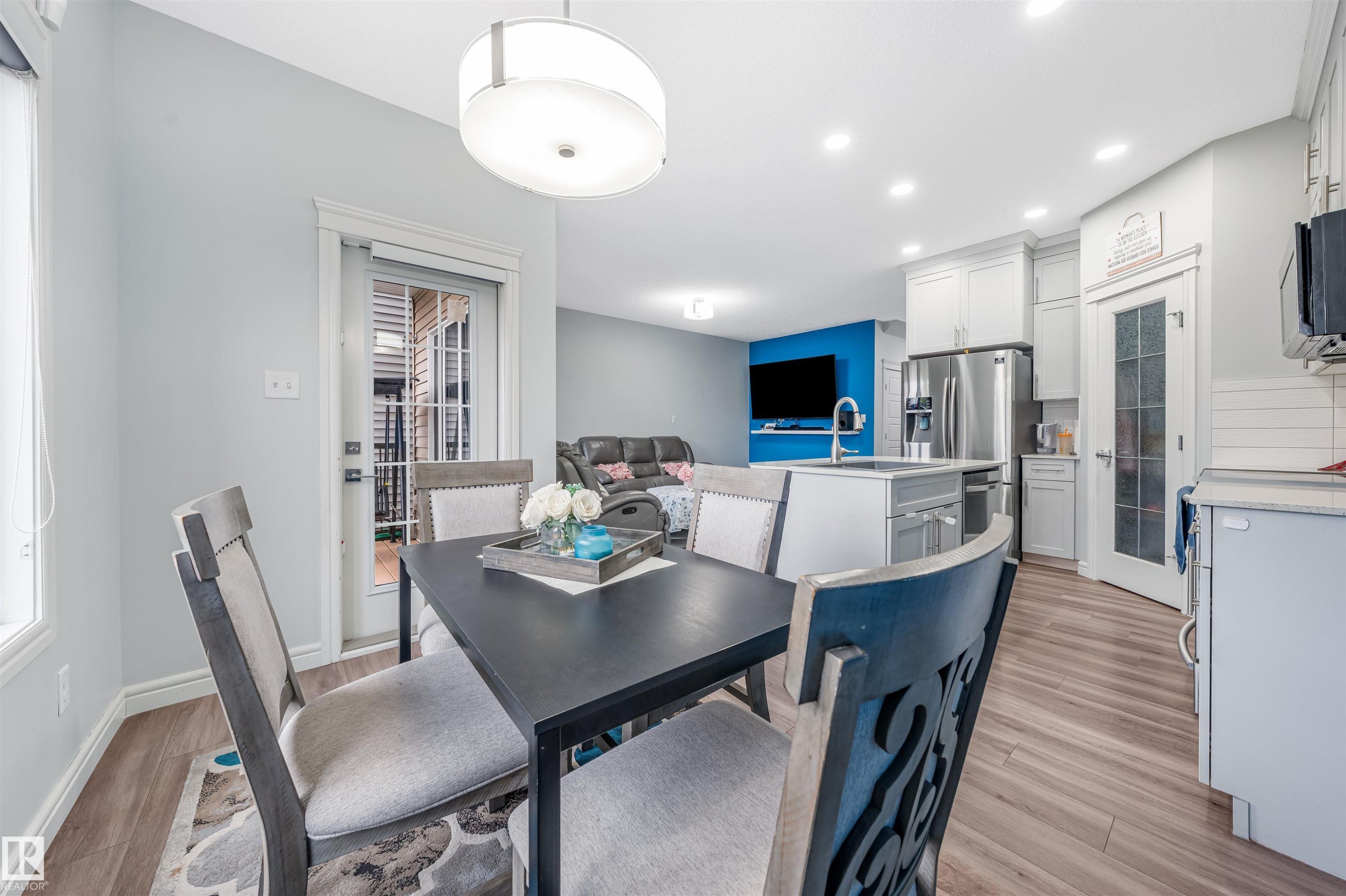 Open-concept living space featuring wood-finish flooring, a kitchen island with integrated sink, stainless steel refrigerator, recessed lighting, and a sliding glass door - 1024 Daniels Loop, Edmonton, AB - Indoor Photo Showing Other Room