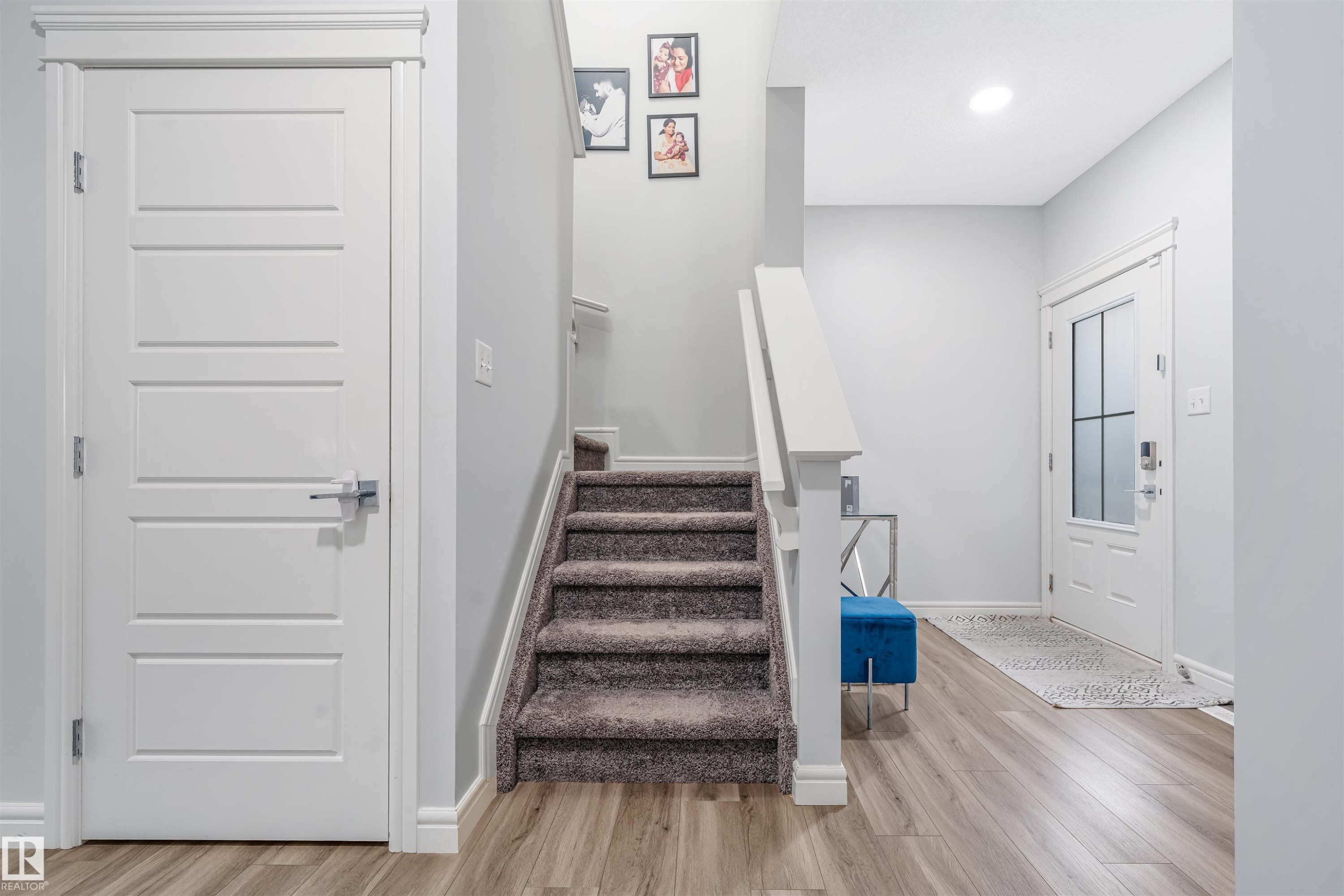 Foyer featuring wood-finish flooring, a carpeted staircase with white railings, a modern paneled interior door, and a front entry door with frosted glass inserts - 1024 Daniels Loop, Edmonton, AB - Indoor Photo Showing Other Room
