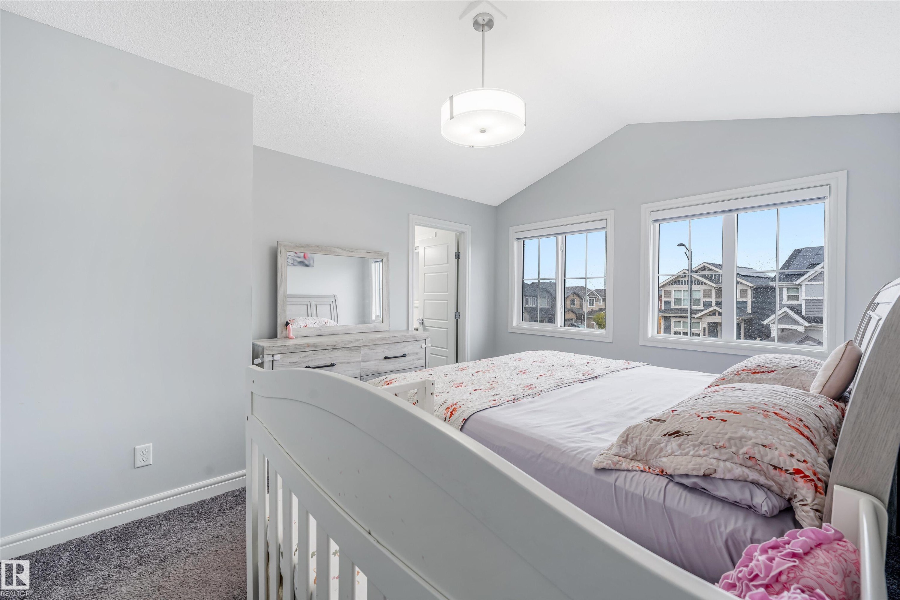 Bedroom featuring vaulted ceilings, plush grey carpeting, two large windows with white trim, and a contemporary ceiling light fixture - 1024 Daniels Loop, Edmonton, AB - Indoor Photo Showing Bedroom