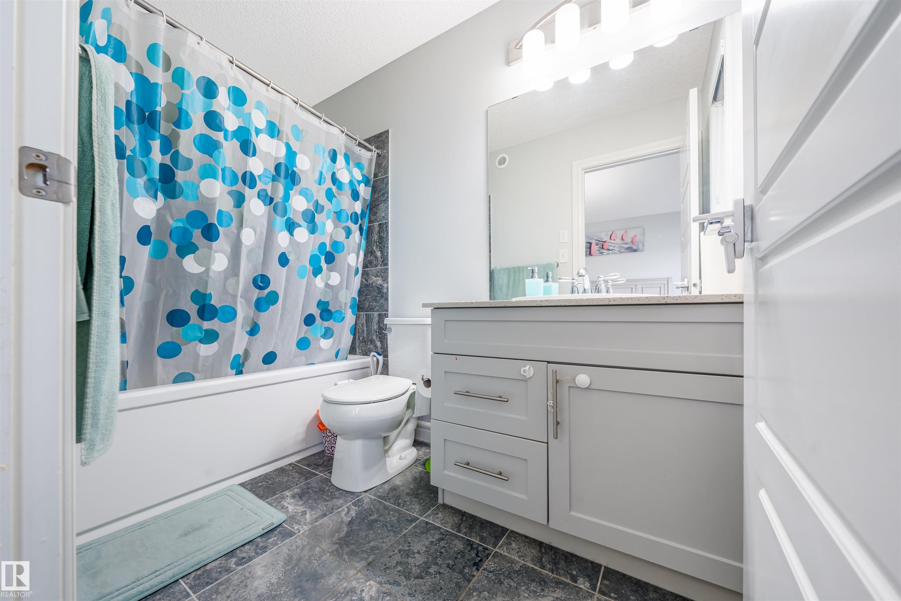 Bathroom featuring a white bathtub, dark-toned tile flooring, and a grey vanity with a light-colored countertop - 1024 Daniels Loop, Edmonton, AB - Indoor Photo Showing Bathroom