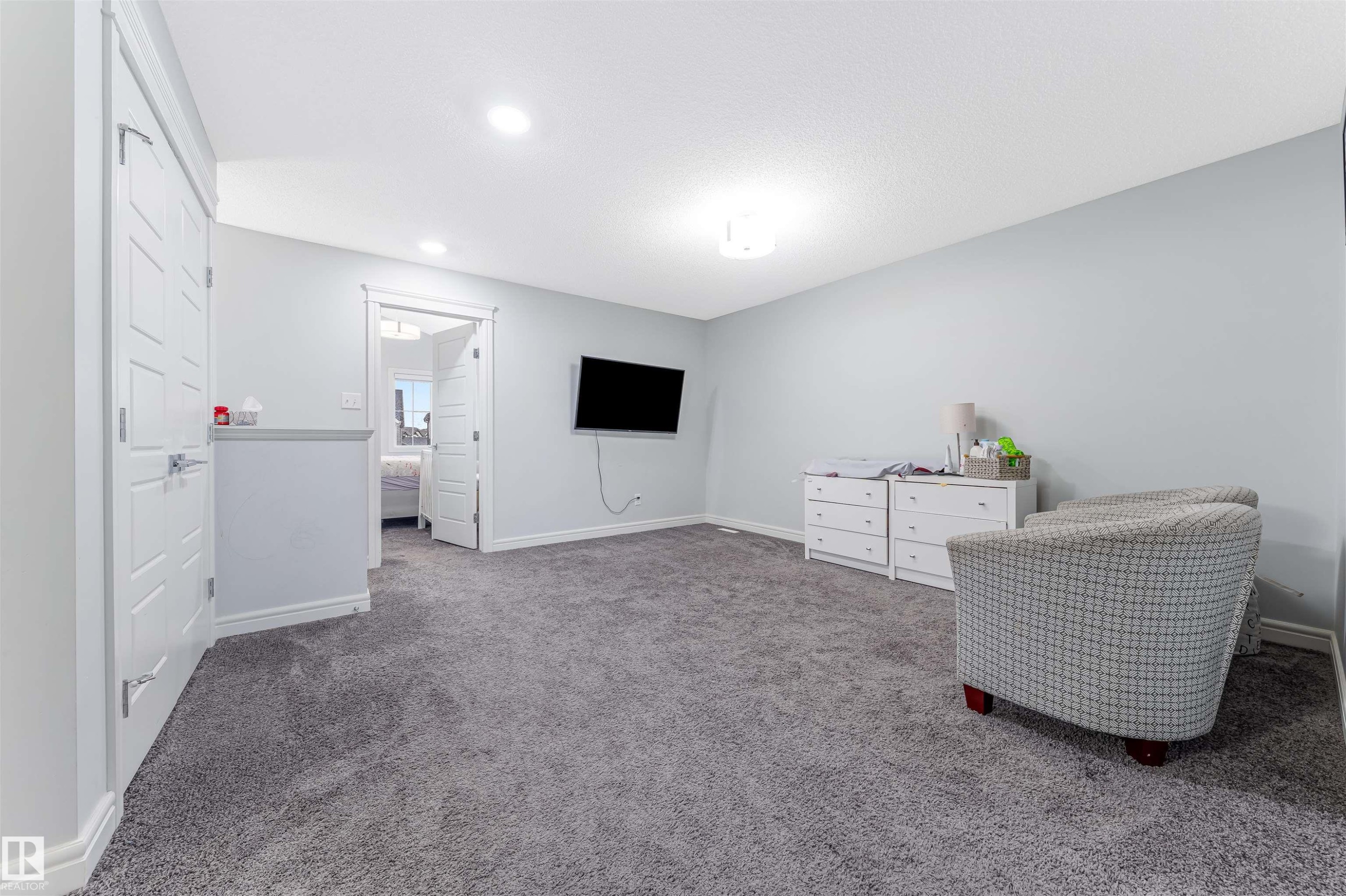 Spacious carpeted room featuring light gray walls, white baseboards, recessed lighting, and a white paneled door - 1024 Daniels Loop, Edmonton, AB - Indoor