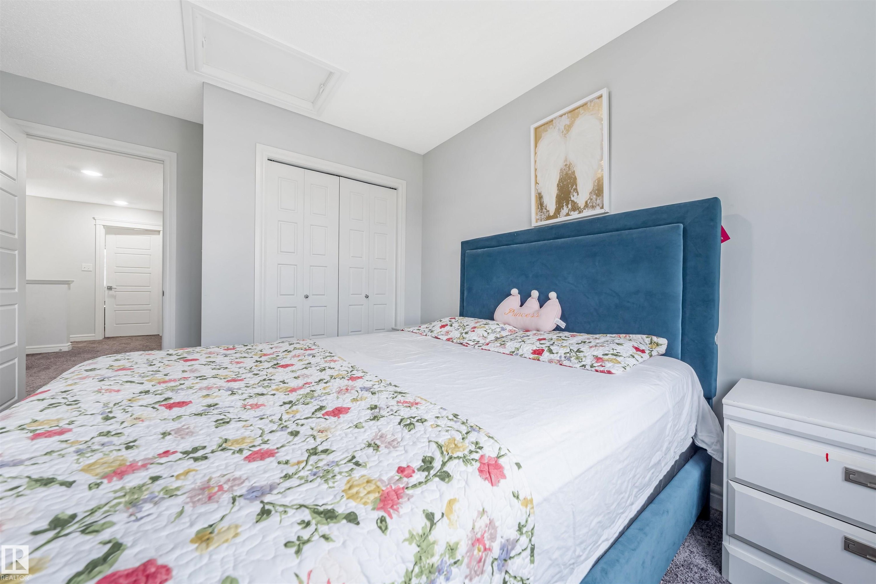 Carpeted room with light gray walls, featuring white bi-fold closet doors and an attic access panel - 1024 Daniels Loop, Edmonton, AB - Indoor Photo Showing Bedroom