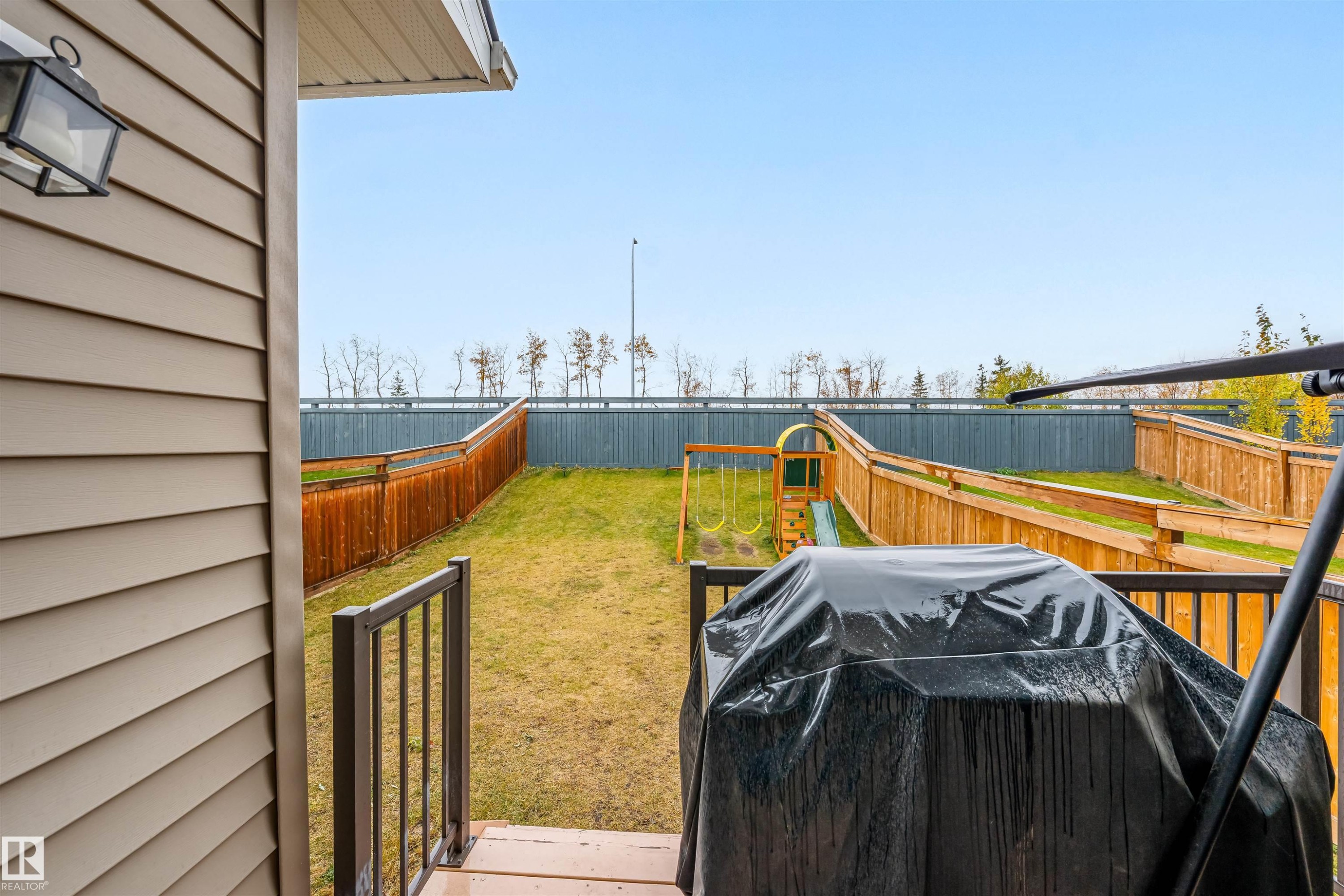 Backyard featuring a wooden deck with black metal railings, a sloped lawn, and a wooden privacy fence - 1024 Daniels Loop, Edmonton, AB - Outdoor With Deck Patio Veranda With Exterior